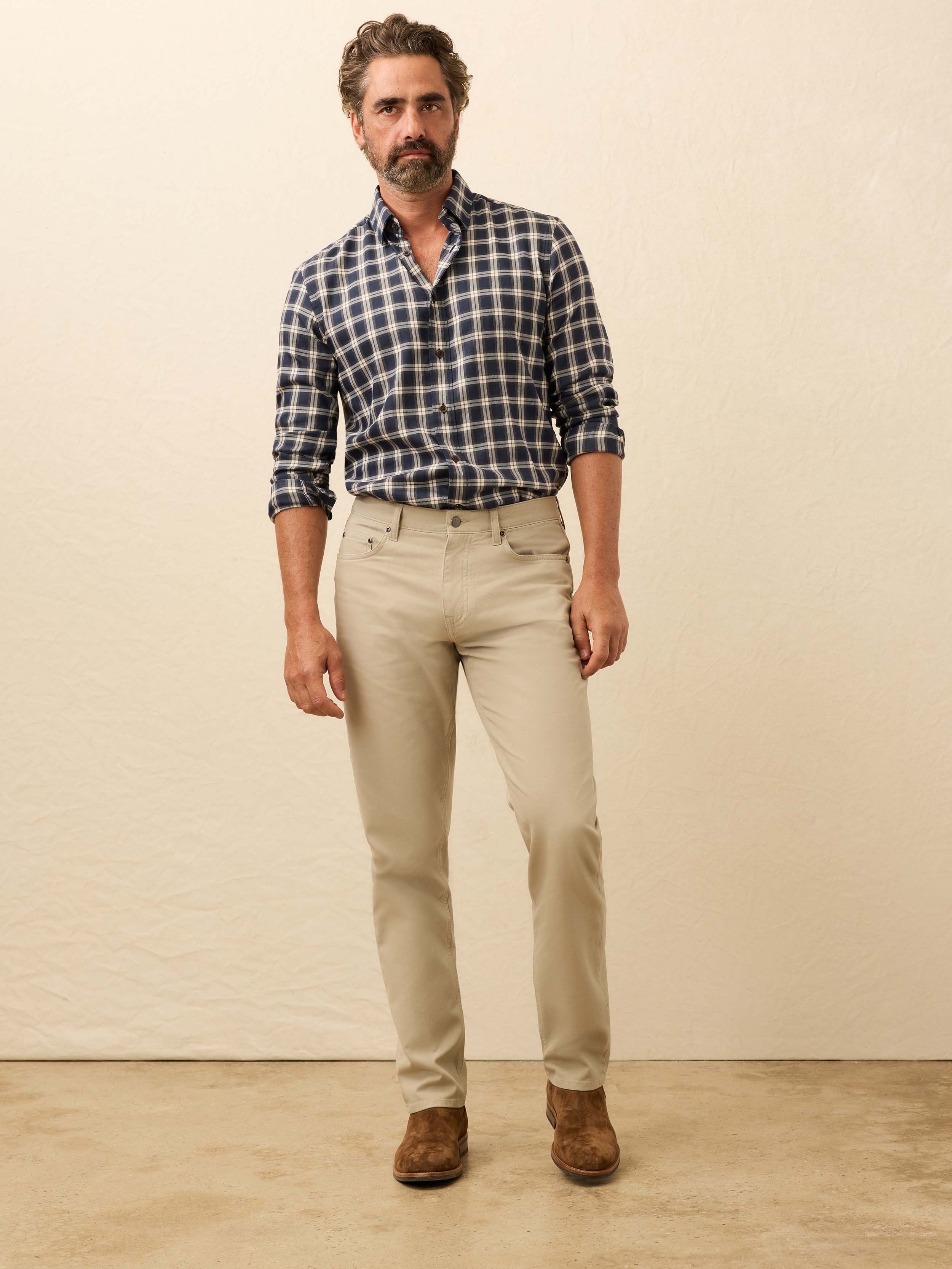 Man is wearing tan twill pants with a blue plaid shirt against a beige background