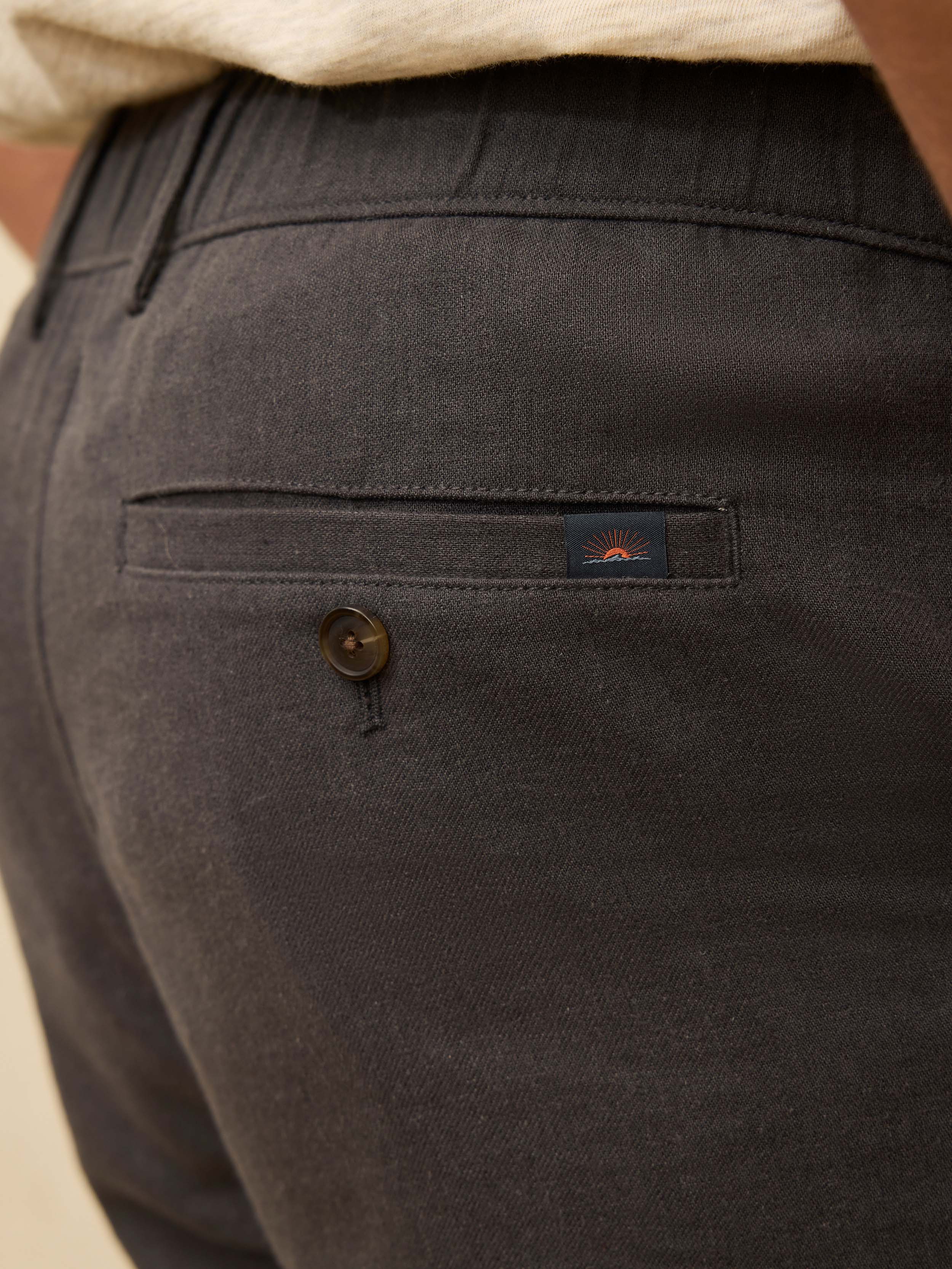 Black linen shorts with a brand logo on the rear buttoned pocket, worn by a man
