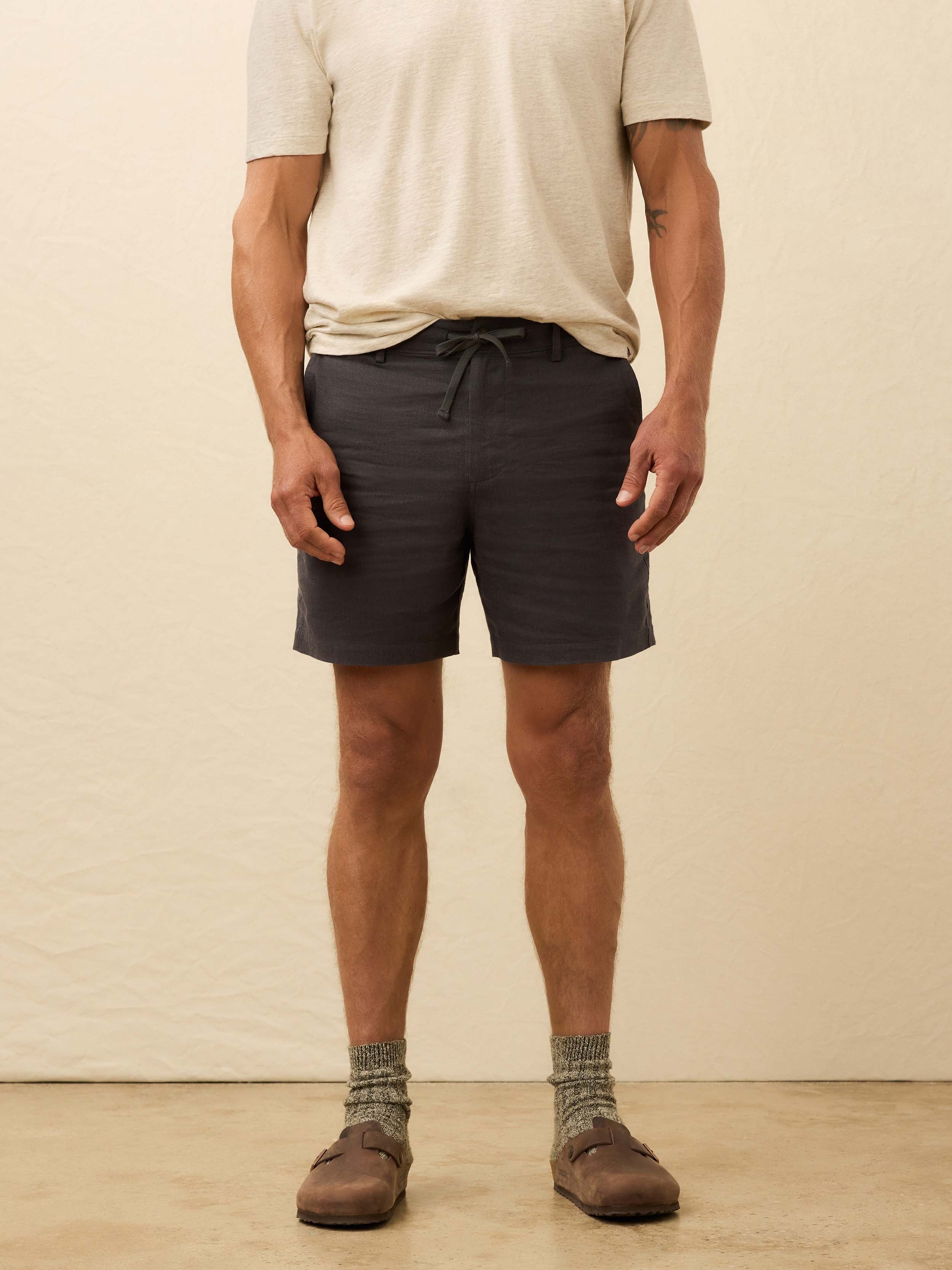 Man wearing black linen shorts against a beige background