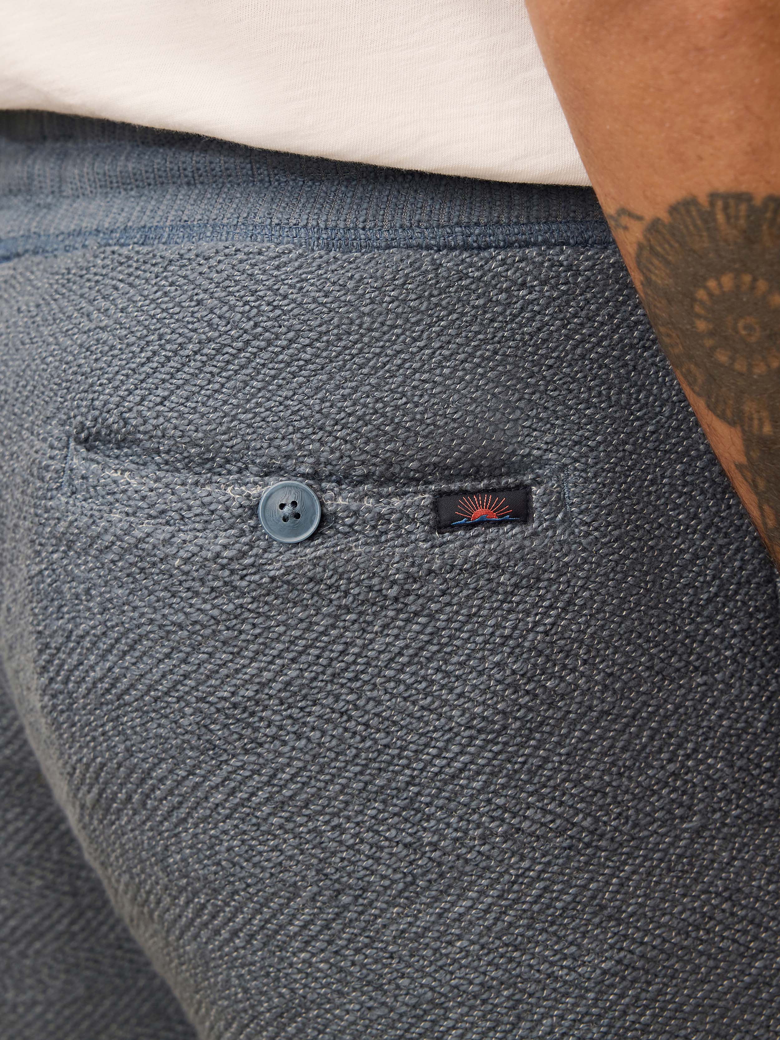 Close up of a man wearing blue shorts a with a branded logo at the rear button pocket