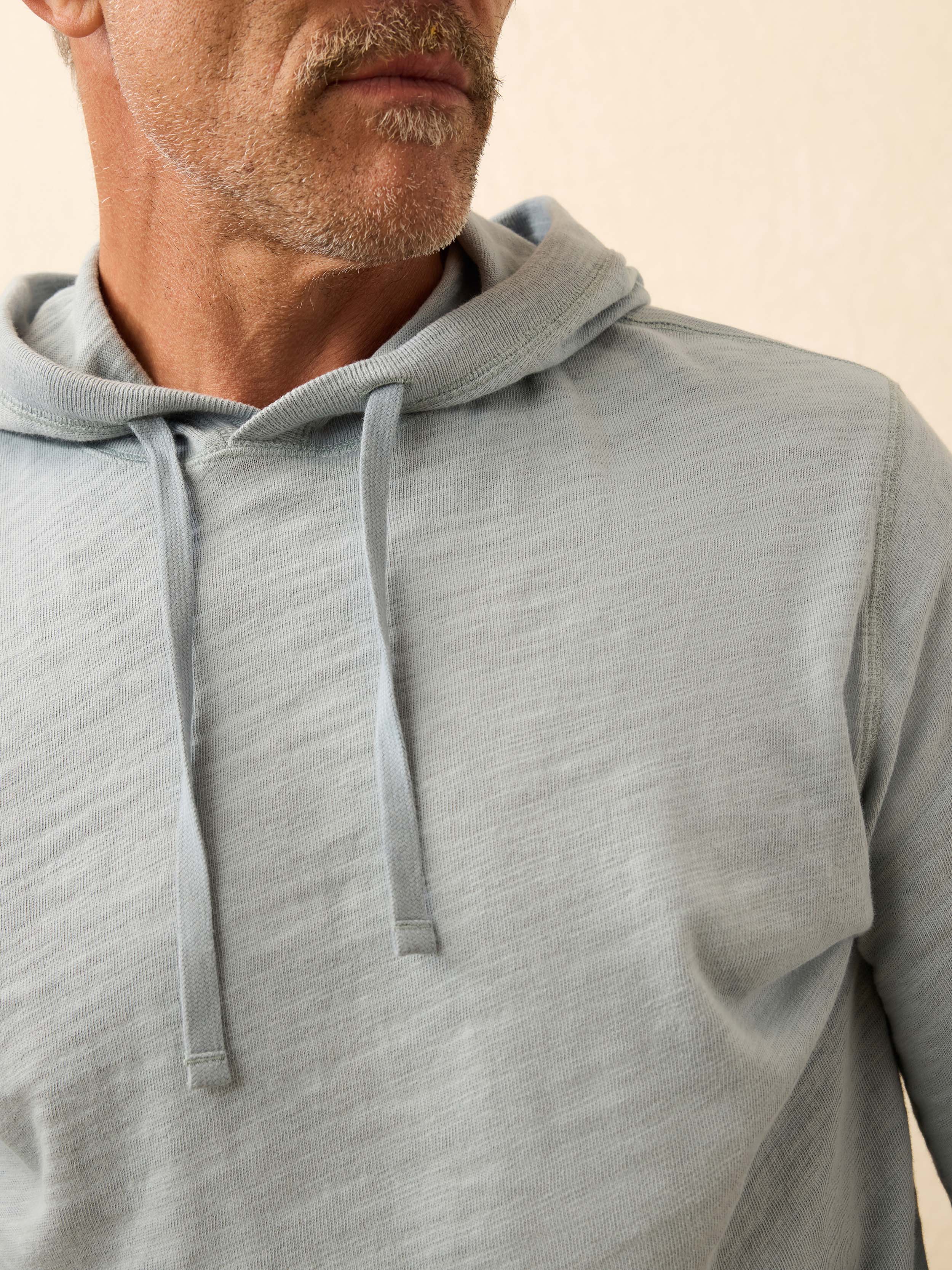 Man wearing a light blue hoodie against a beige wall