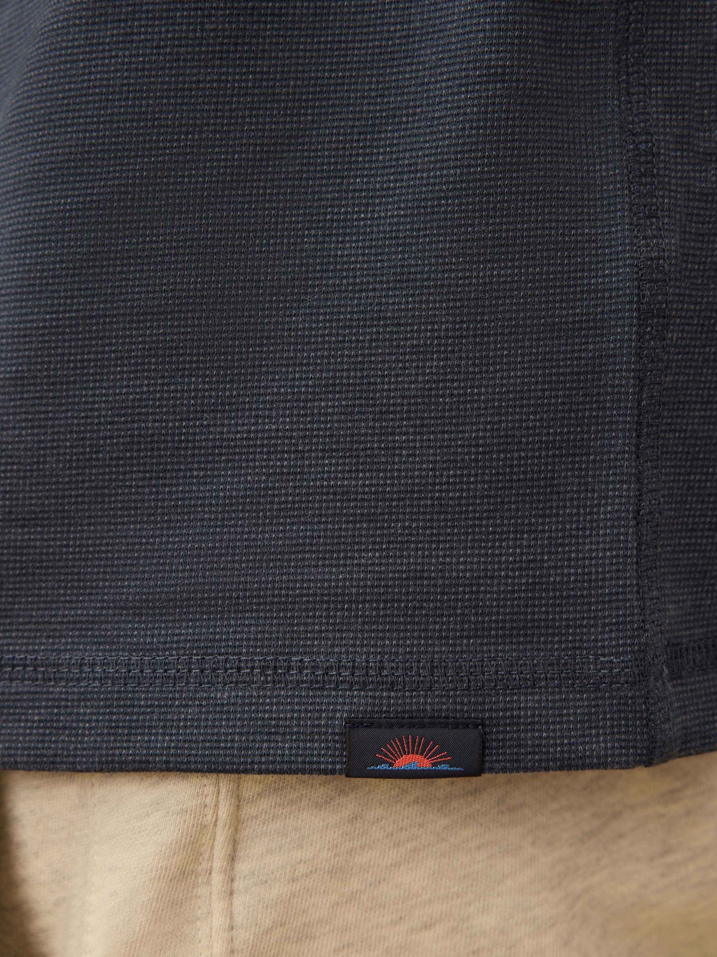 Close-up of a navy blue henley shirt with a brand label on the hem