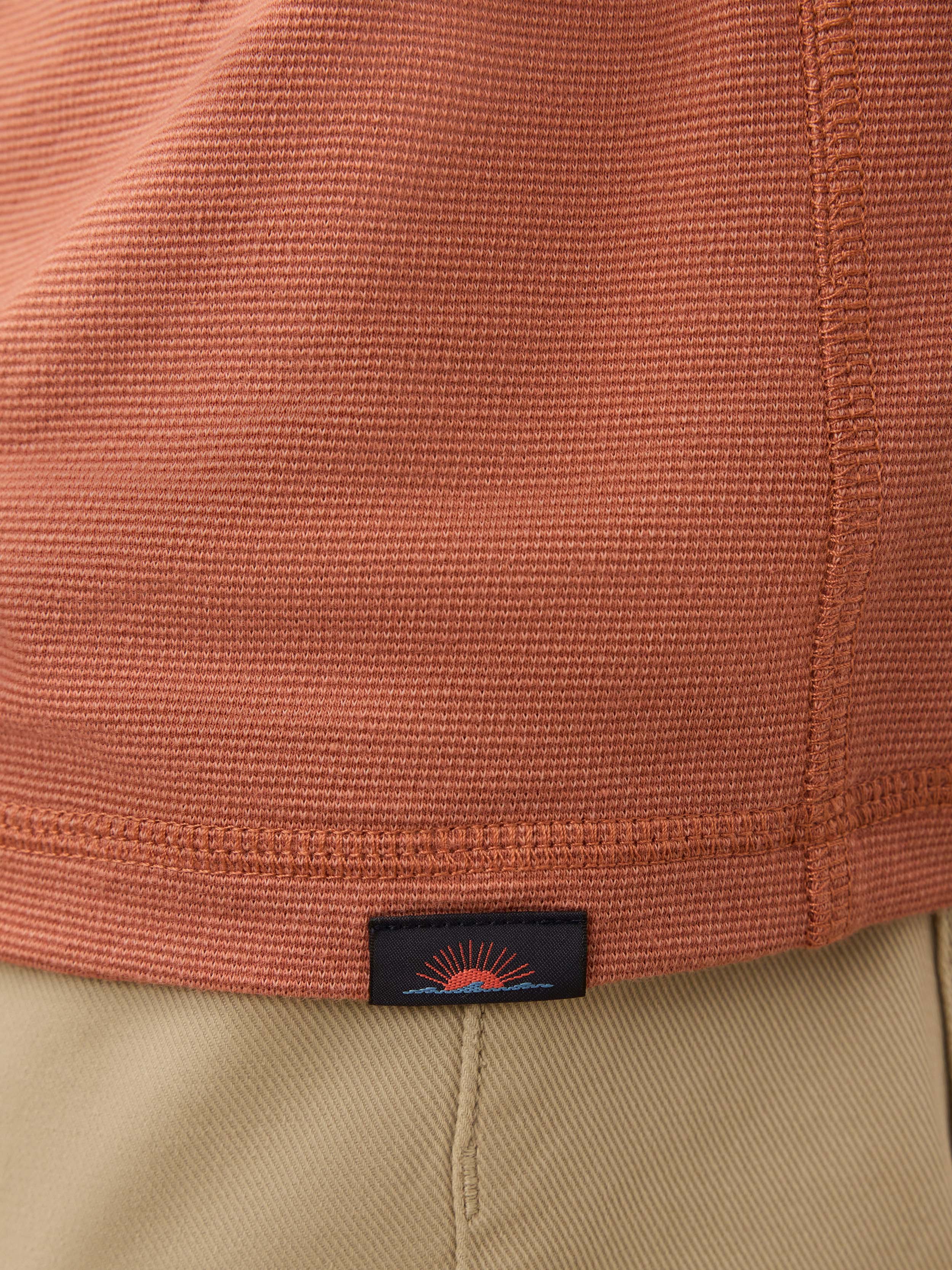 Close-up of a salmon henley shirt with a brand logo on the hem