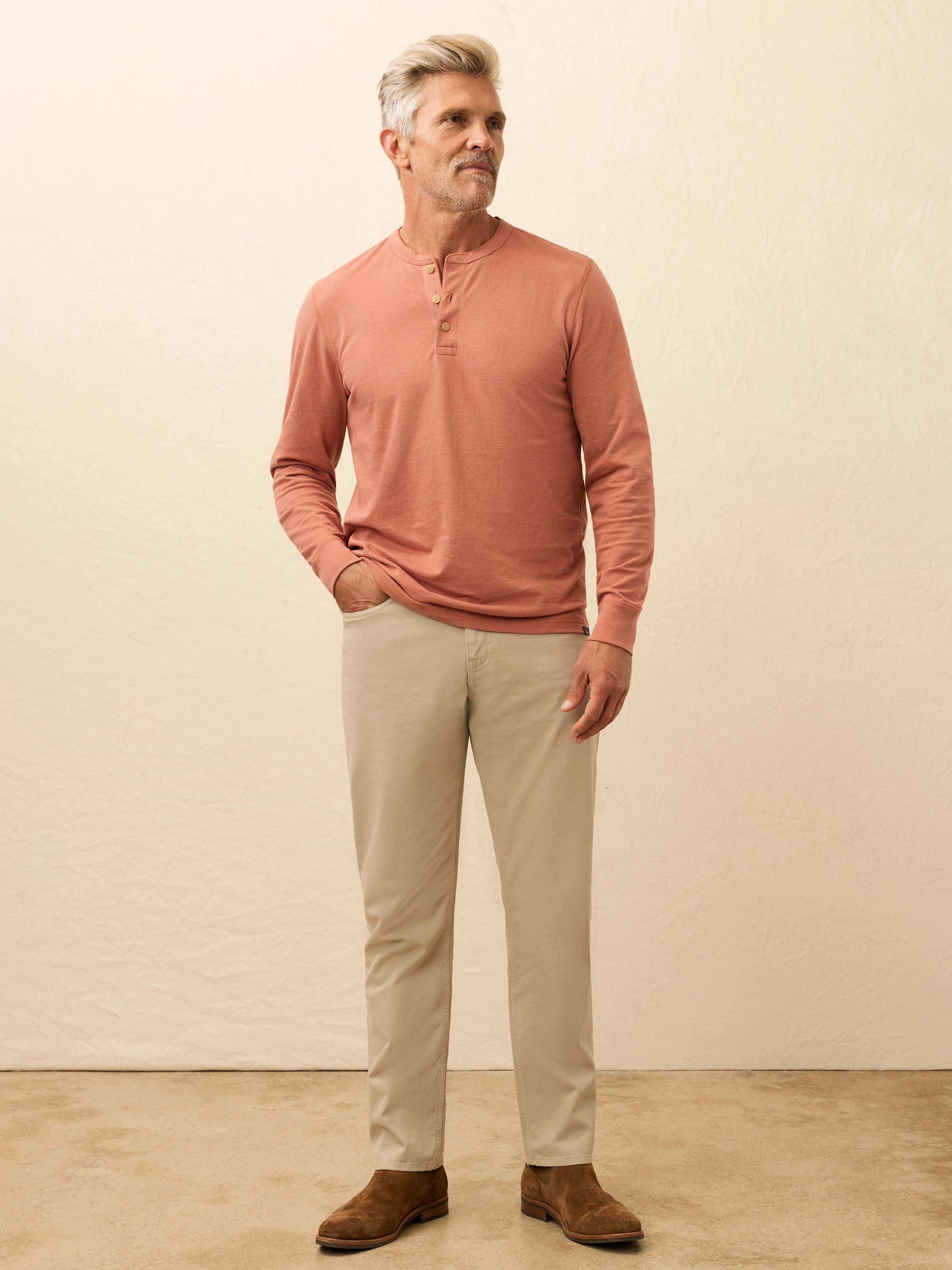 Man wearing a salmon color long sleeve henley shirt against a beige background