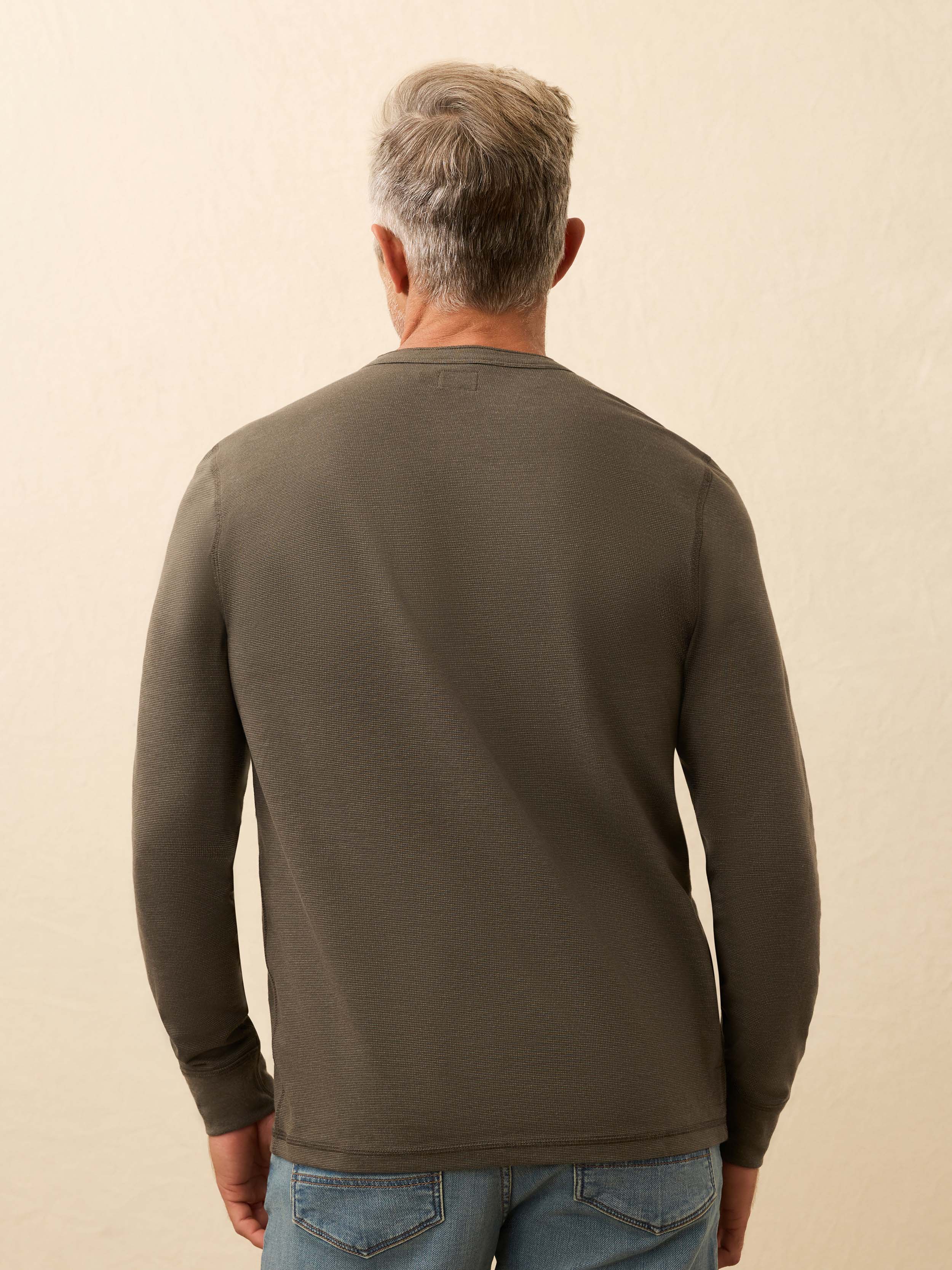 Man wearing a brown long sleeve henley shirt against a beige background