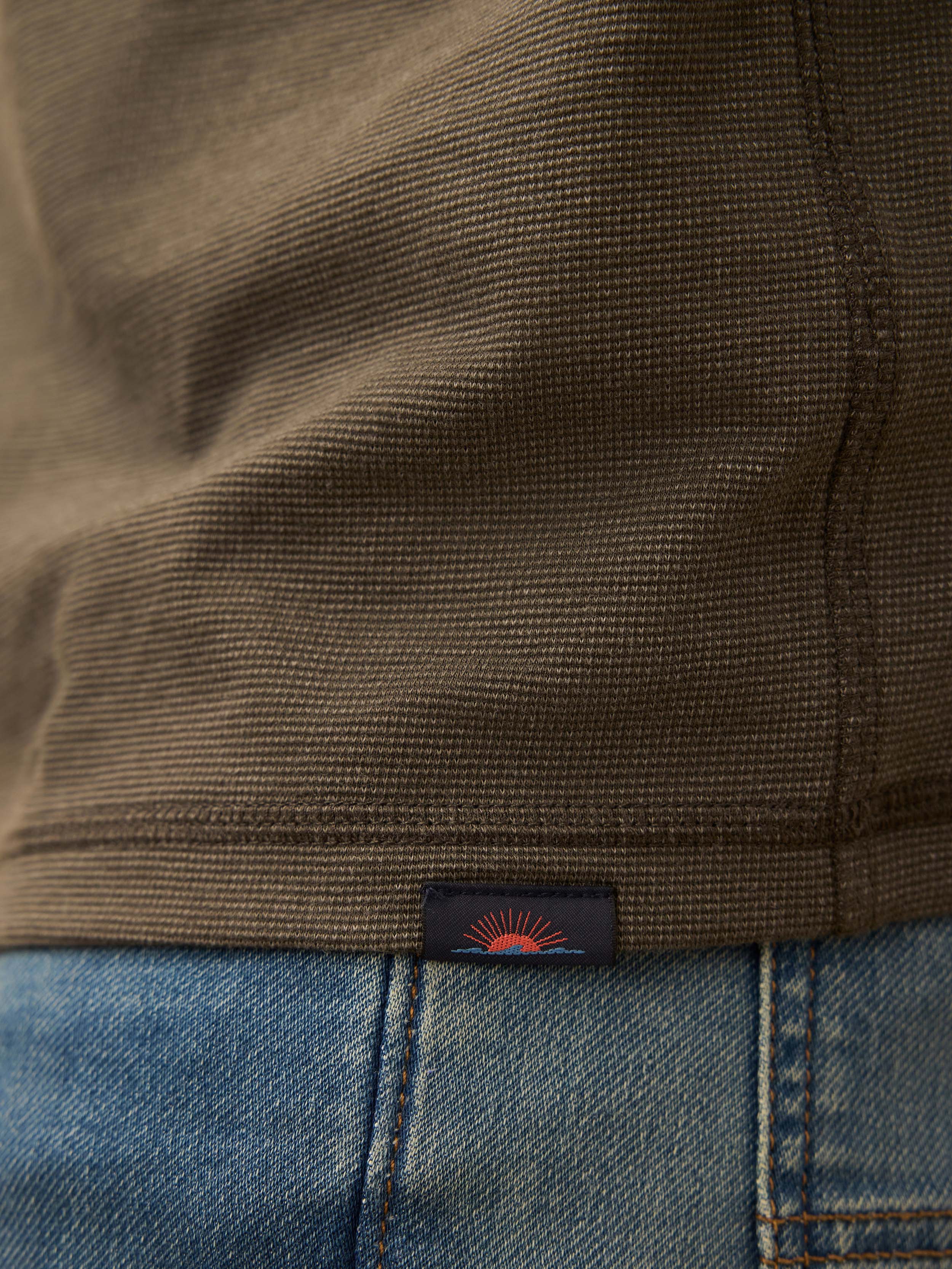 Close-up of a brown henley shirt with a brand label on the hem