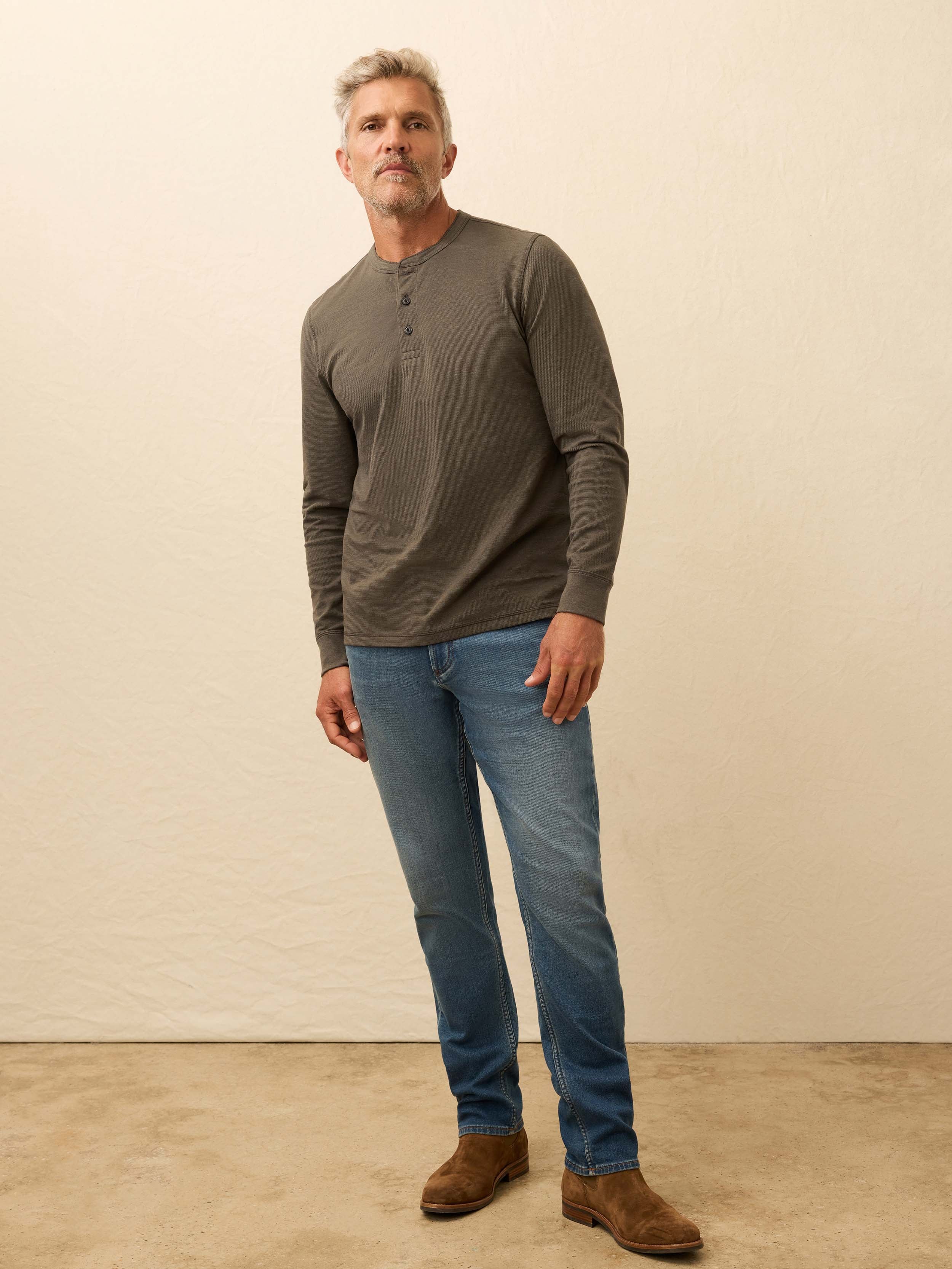 Man wearing a brown long sleeve henley shirt against a beige background
