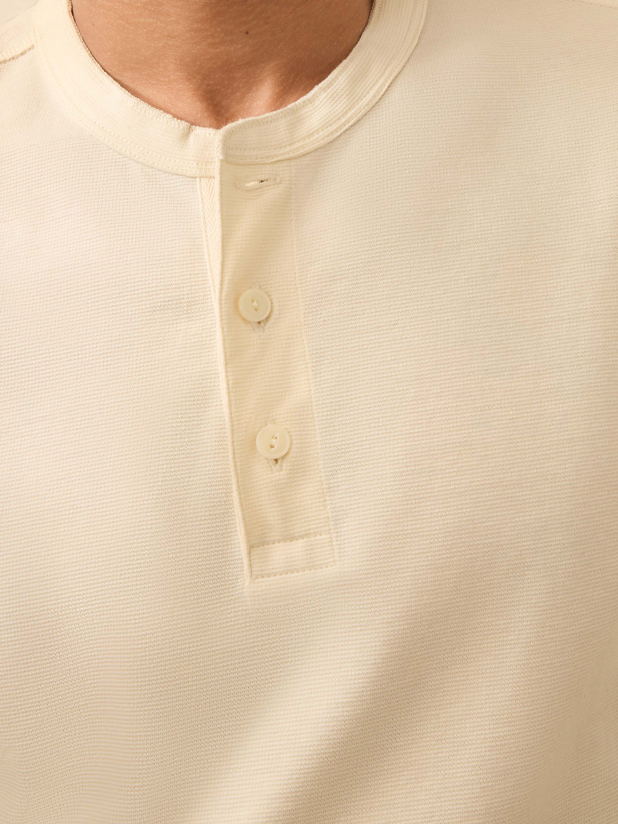 Close-up of a cream colored long sleeve henley shirt with buttons 