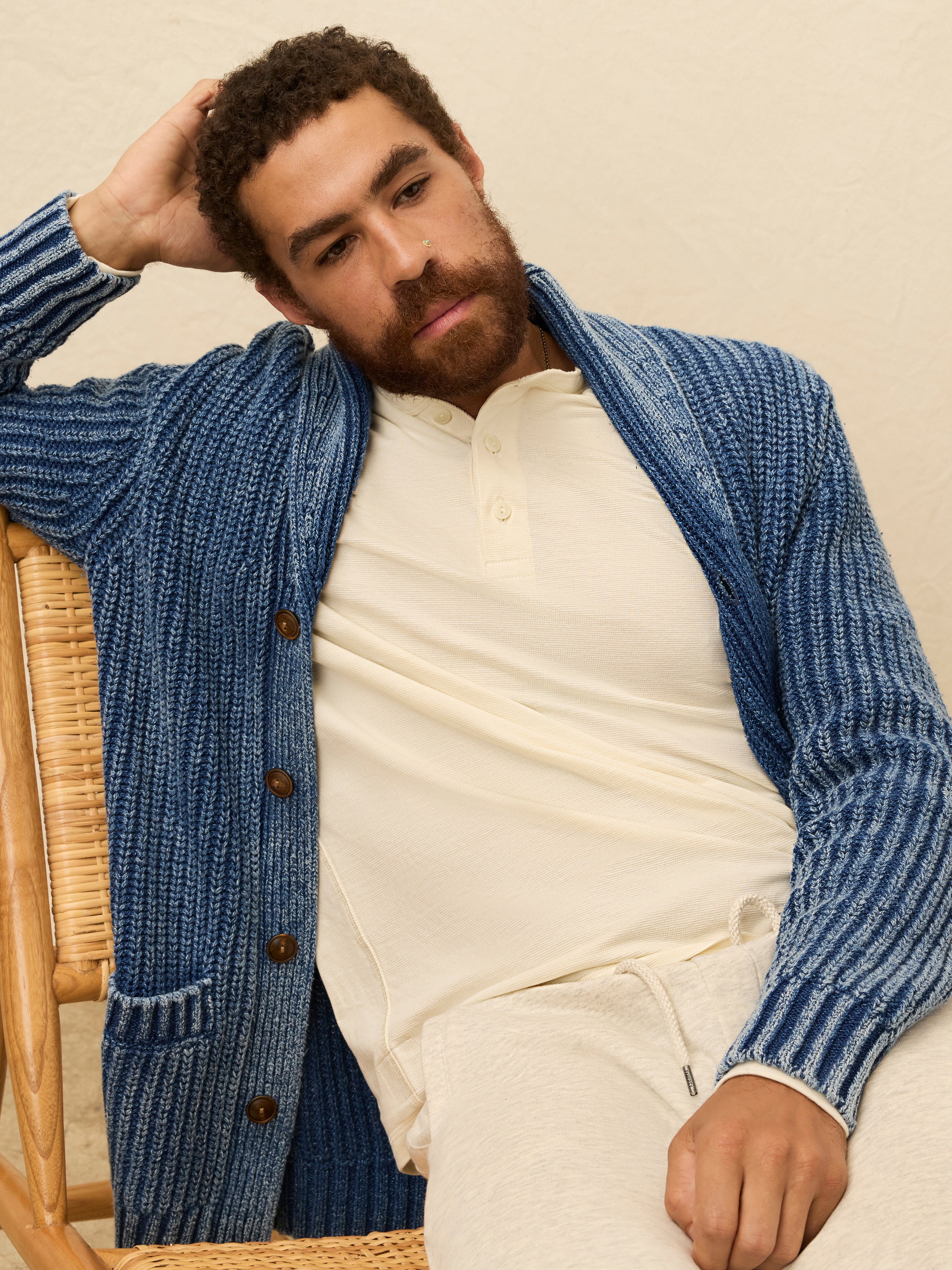 Man wearing a blue knitted cardigan over a cream colored long sleeve henley shirt