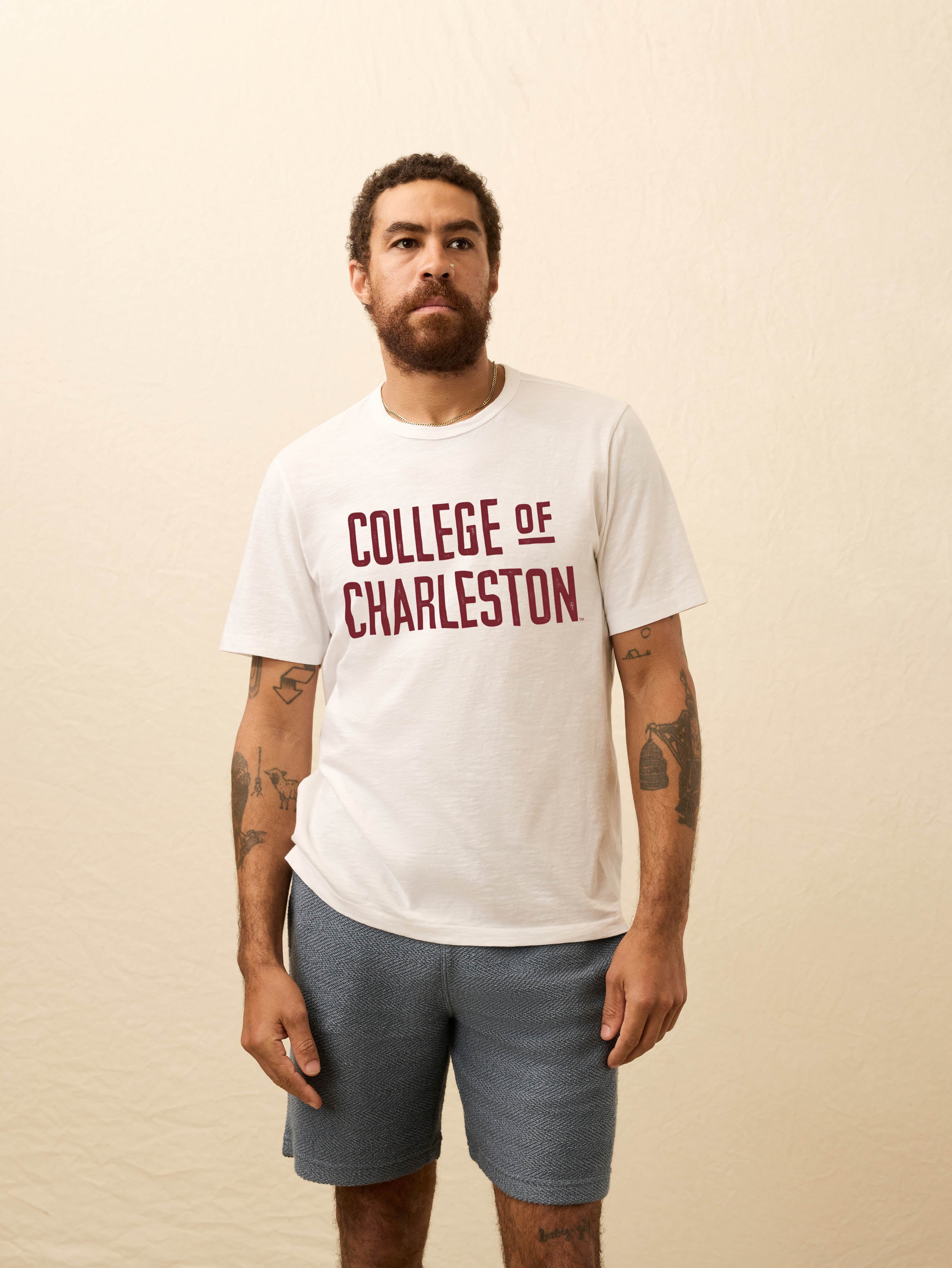 Man wearing a white short sleeve t-shirt with College of Charleston graphic on a beige background
