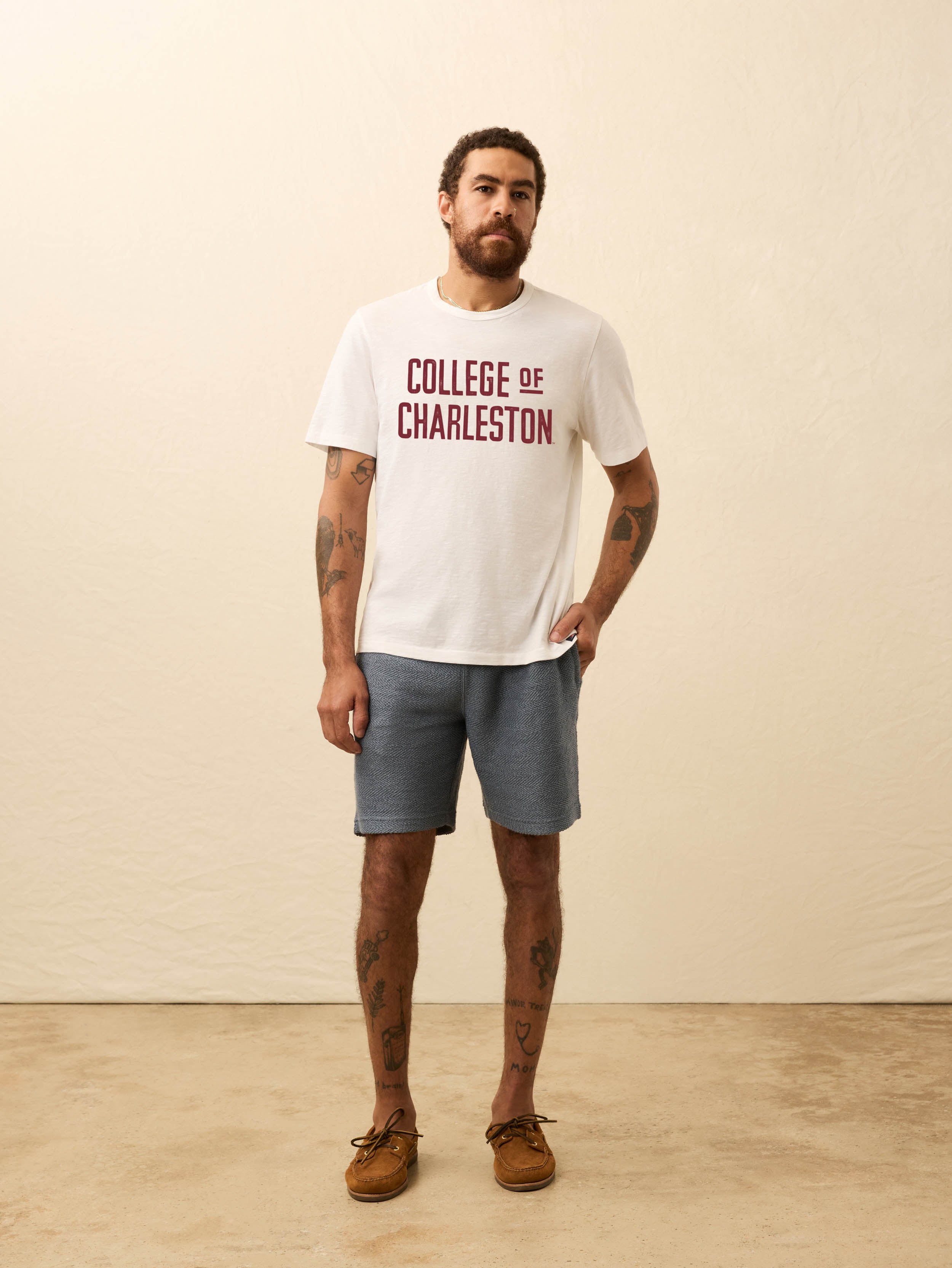 Man wearing a white short sleeve t-shirt with College of Charleston graphic on a beige background