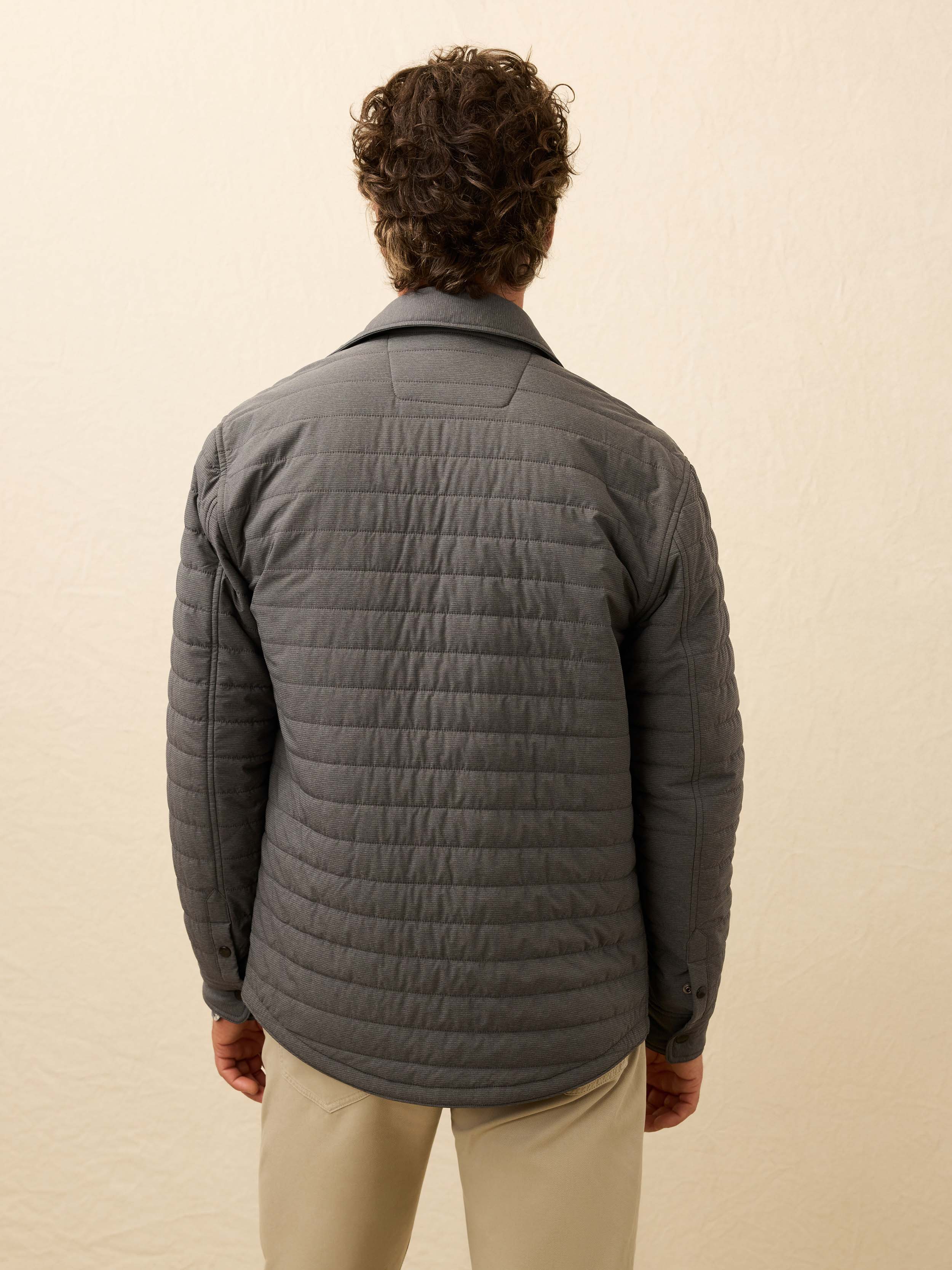 Man wearing a gray quilted jacket against a beige background