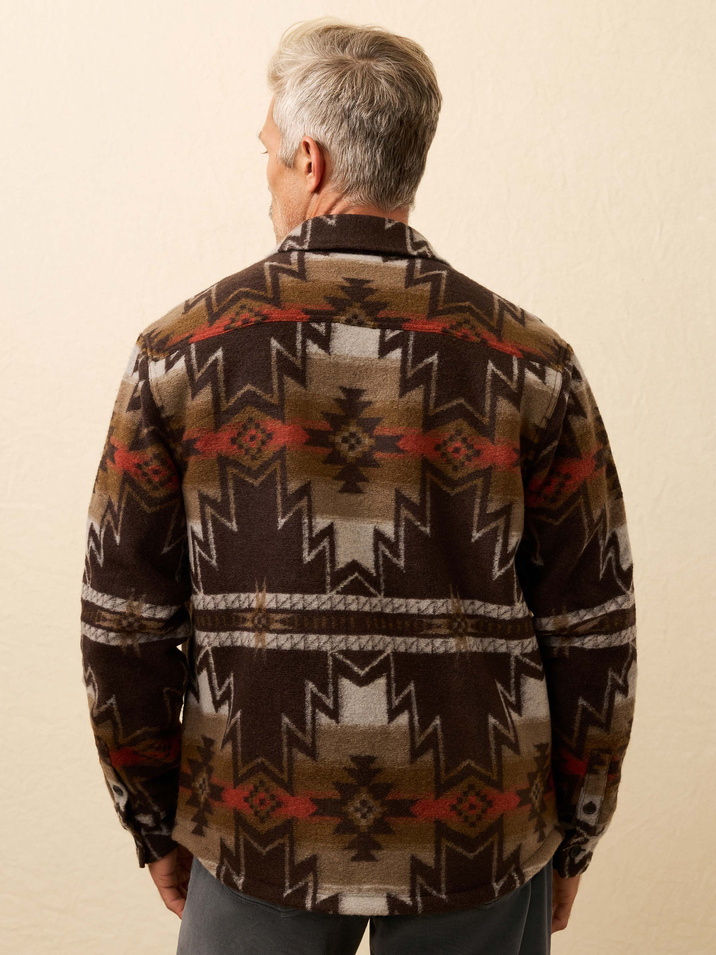 Man wearing a Native American patterned jacket with a beige background