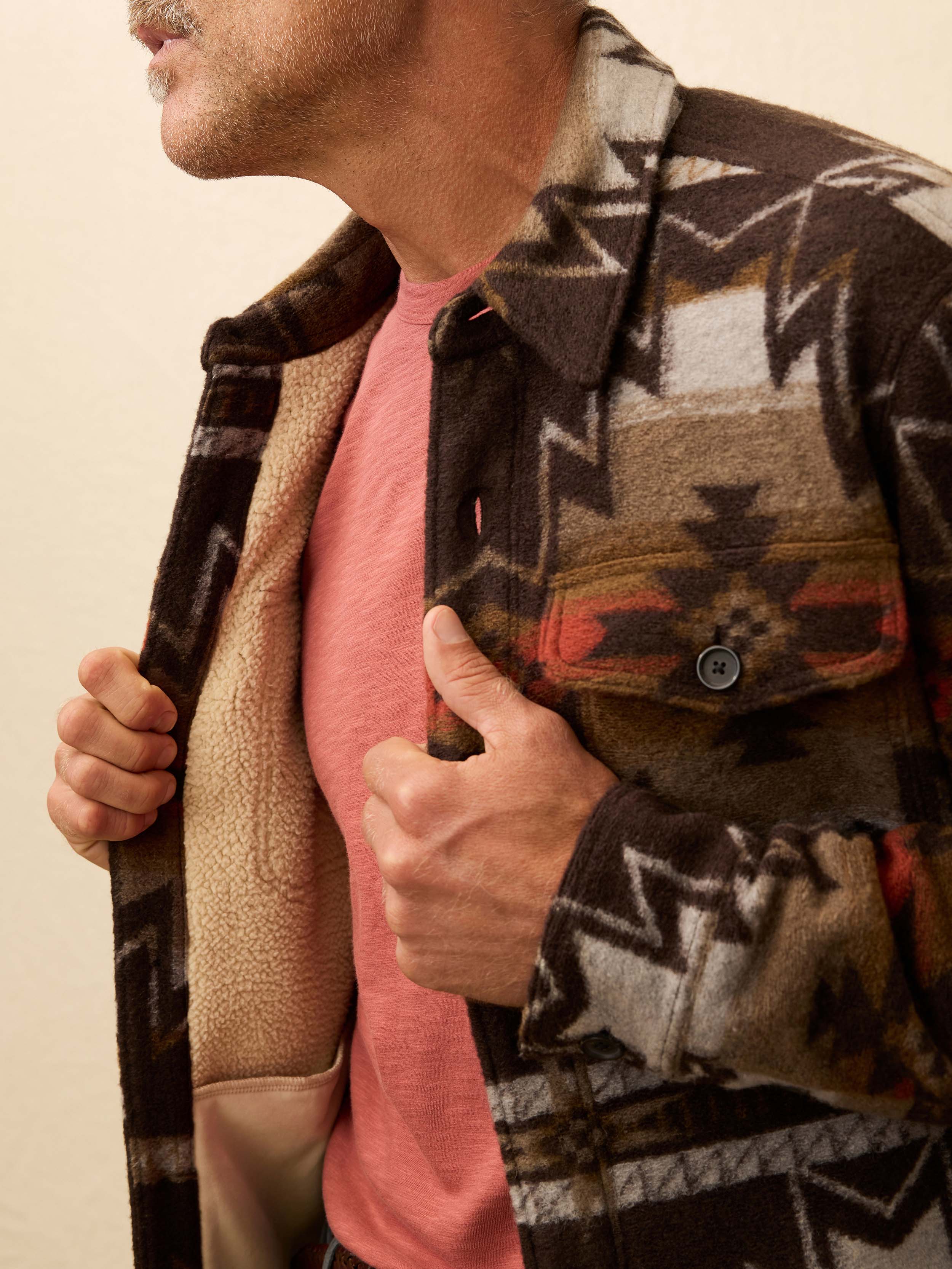 Man wearing a Native American patterned jacket with a beige background