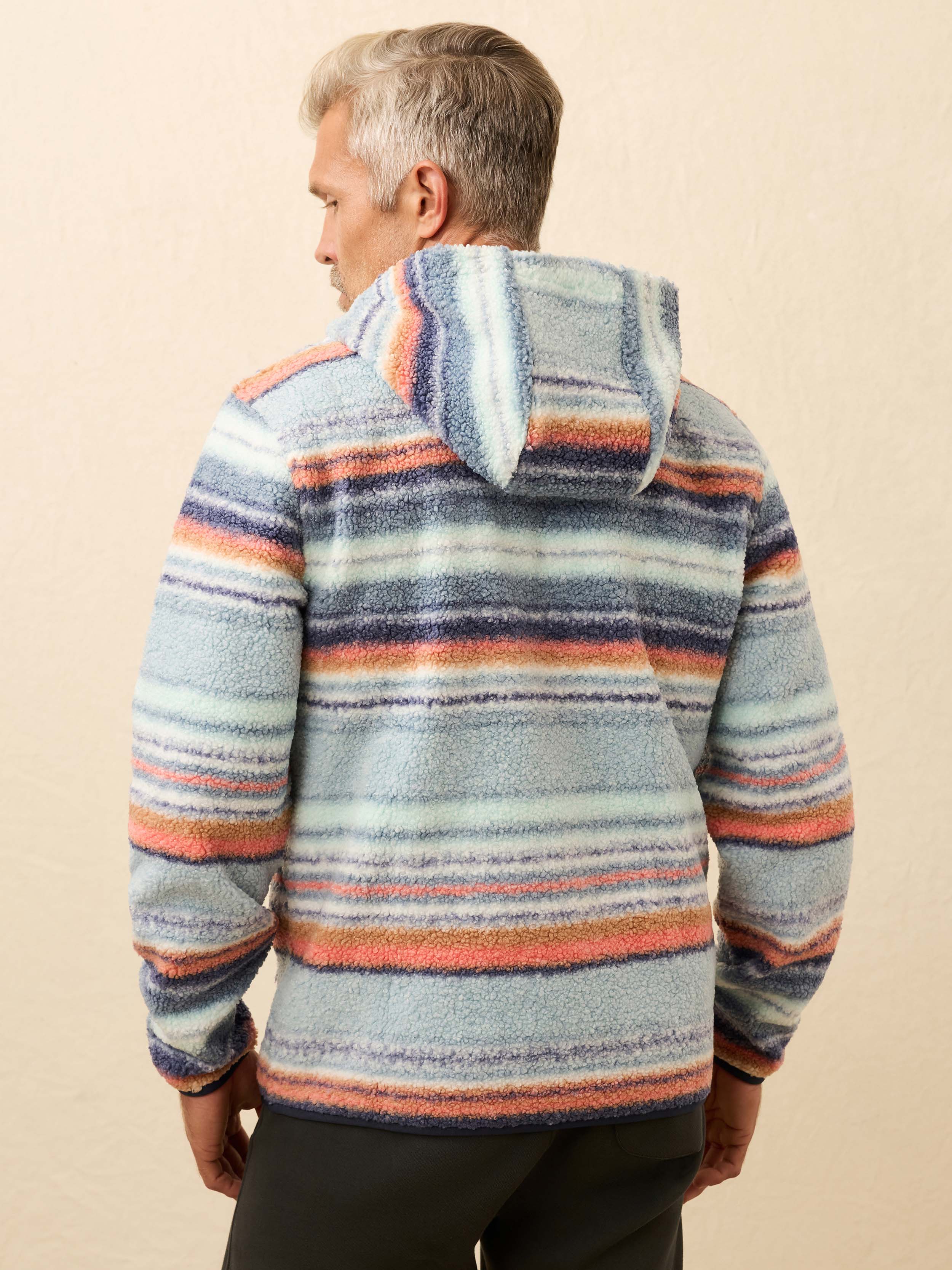 Man wearing a colorful striped fleece hoodie against a beige wall