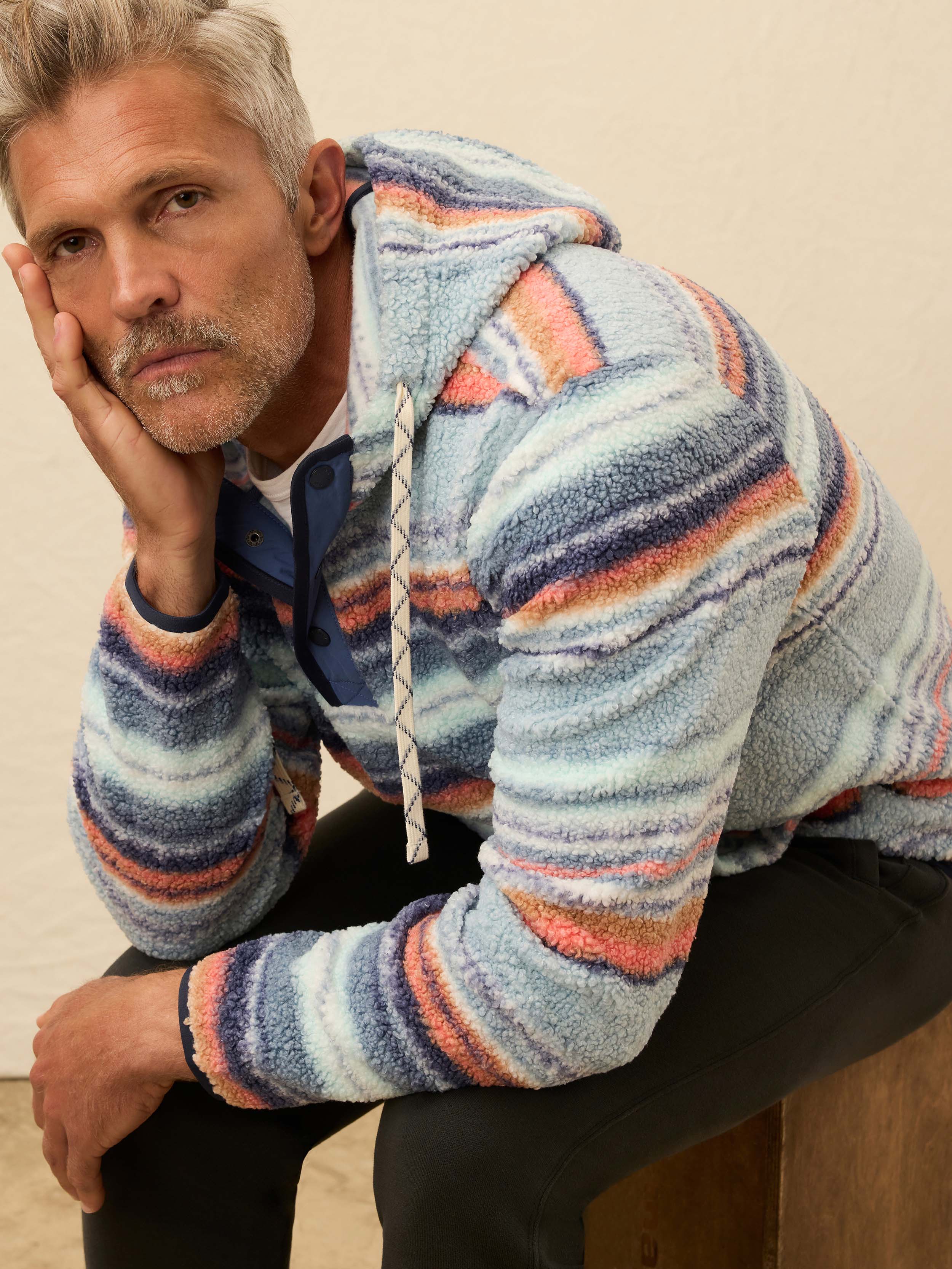Man wearing a colorful striped fleece hoodie against a beige wall
