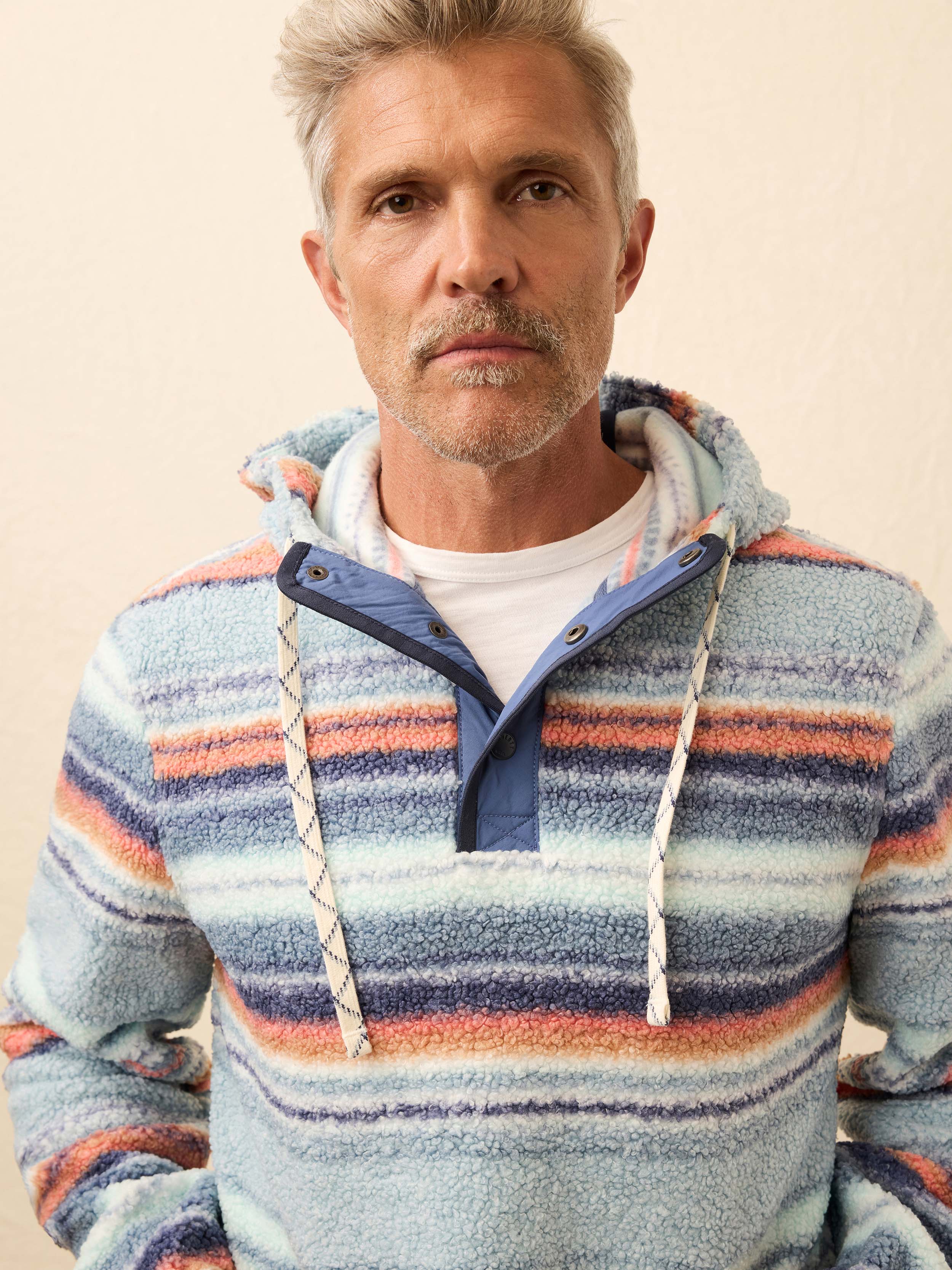 Man wearing a colorful striped fleece hoodie against a beige wall