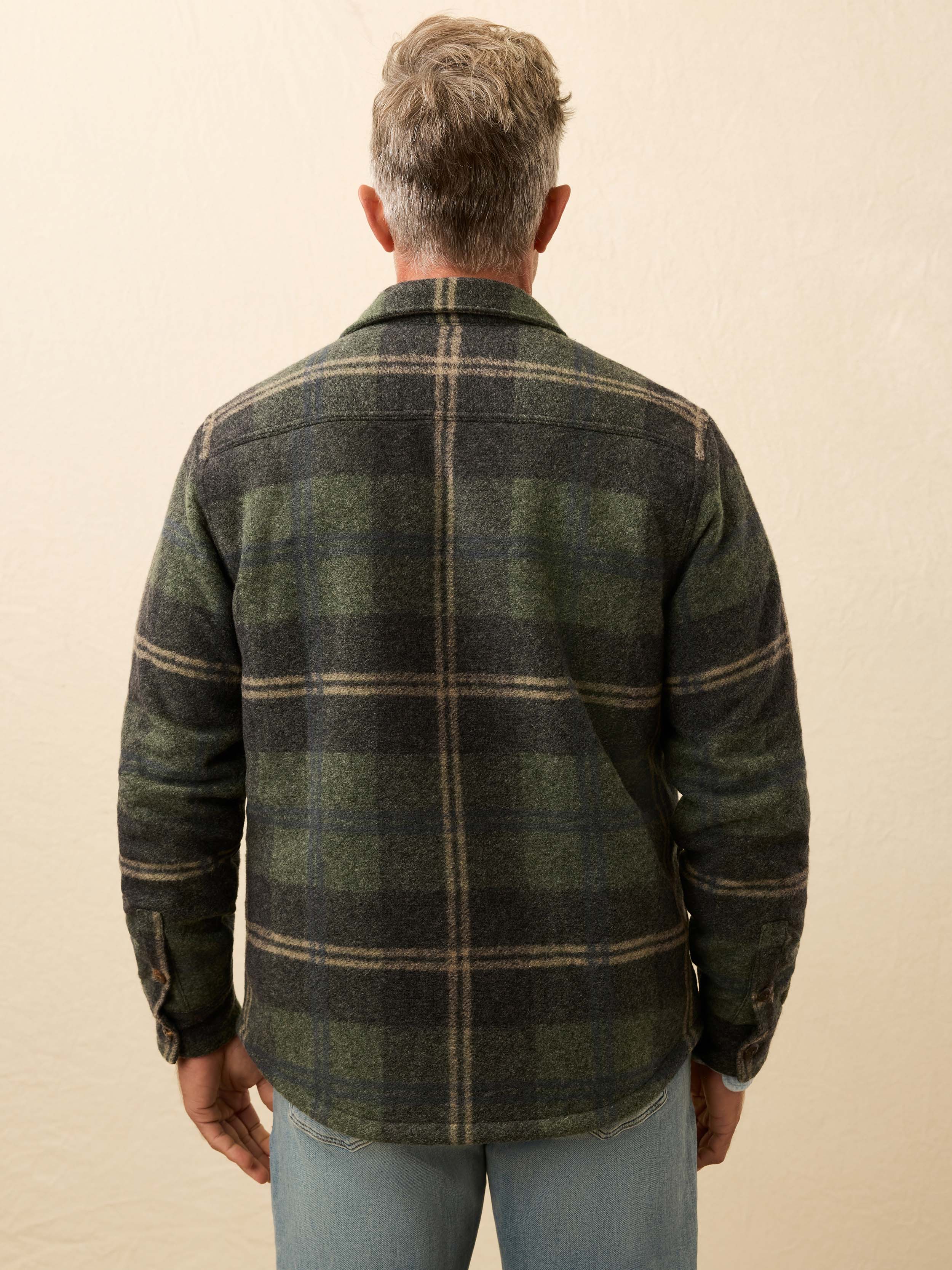 Man wearing a green plaid jacket over a blue shirt on a beige background