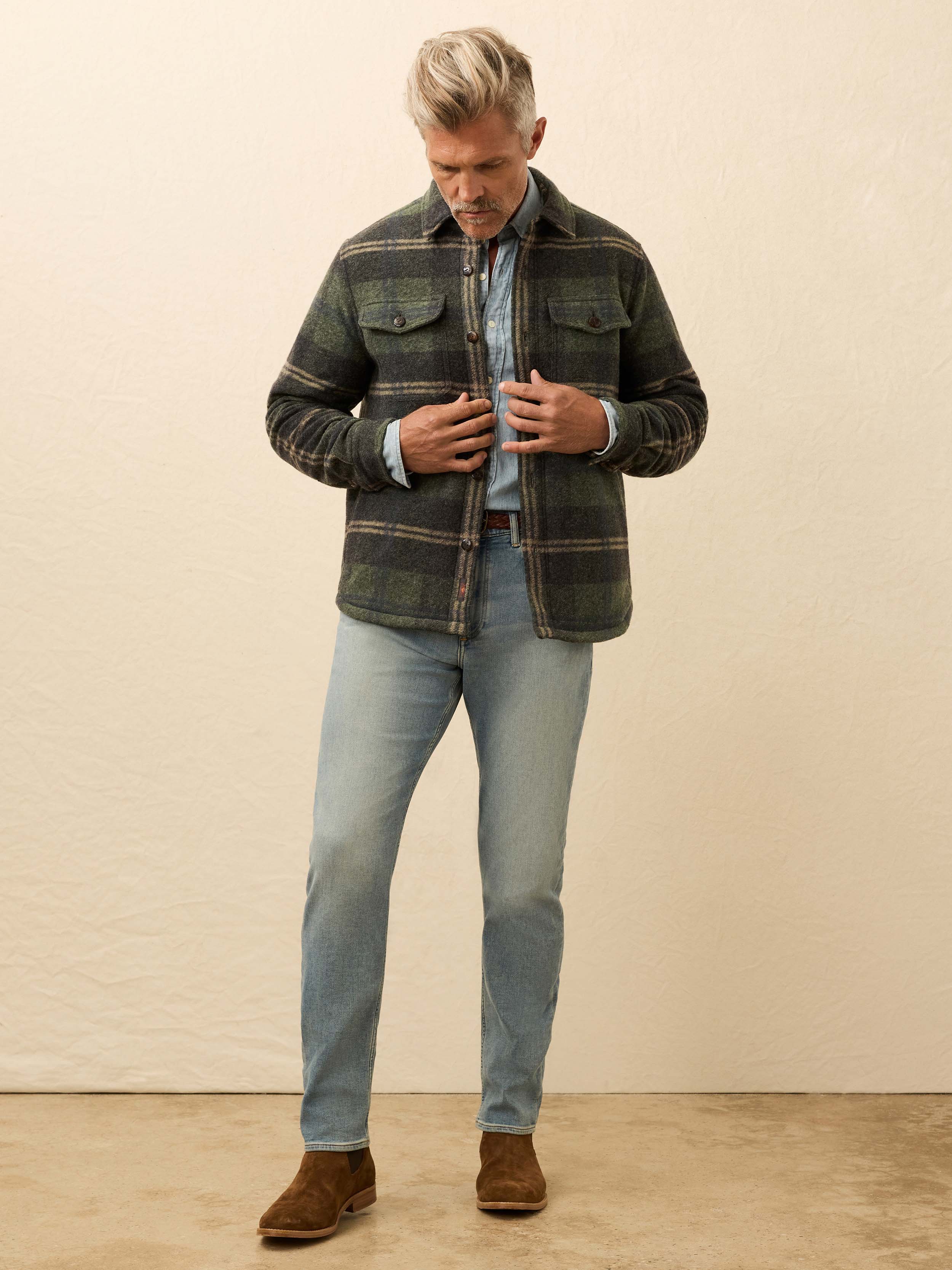 Man wearing a green plaid jacket over a blue shirt on a beige background