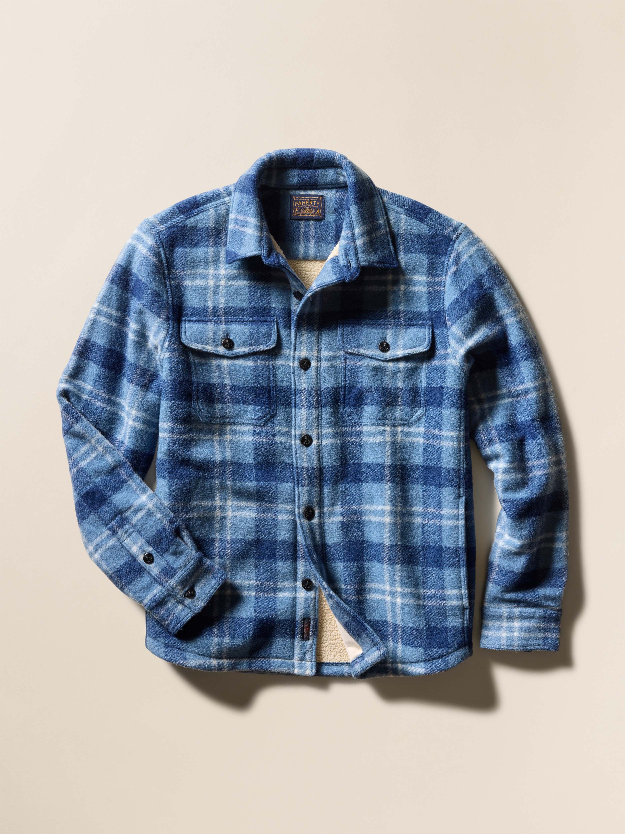 Blue plaid flannel shirt jacket with fleece lining against a beige background