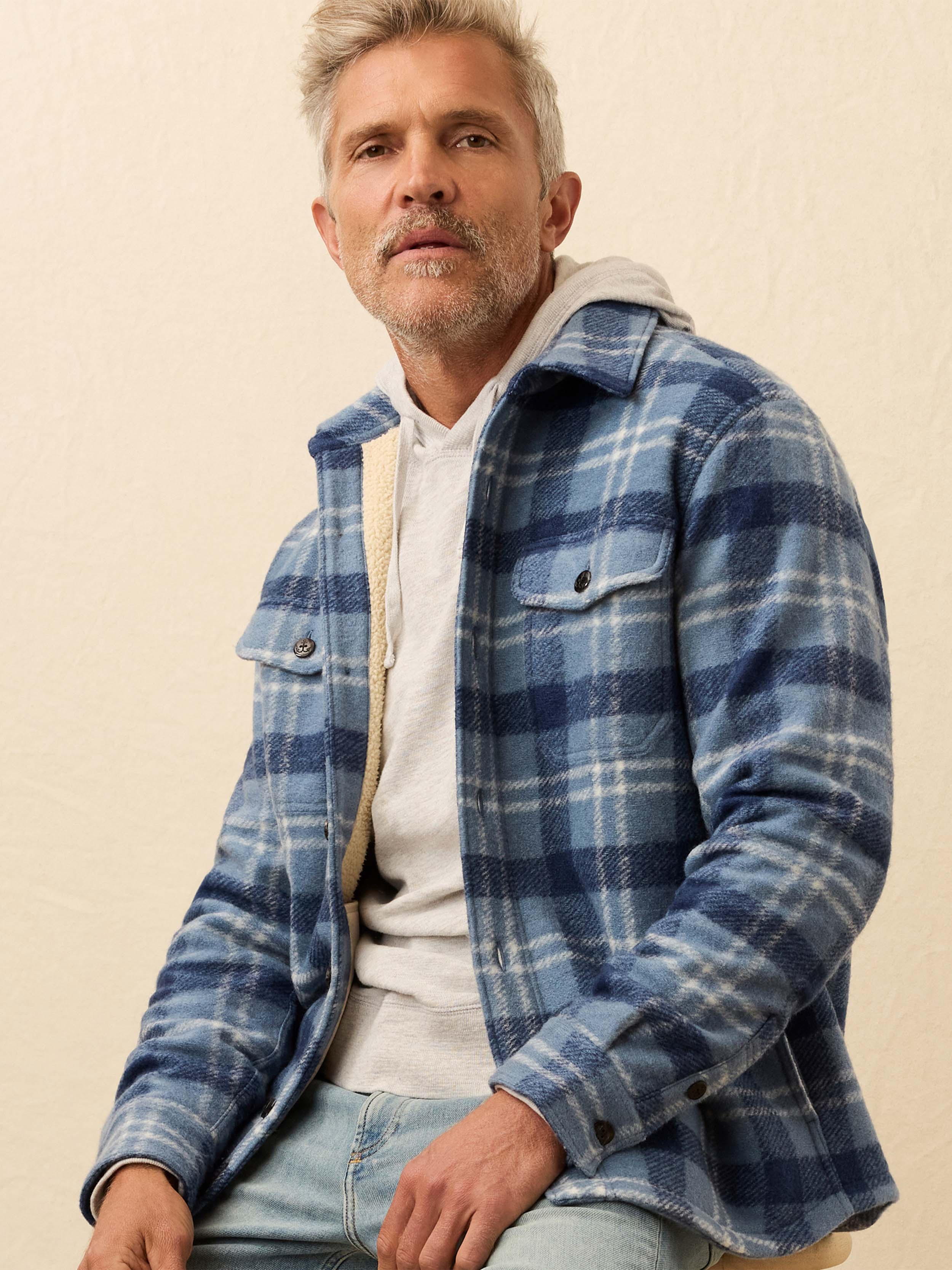 Man wearing a blue flannel shirt jacket against a beige background