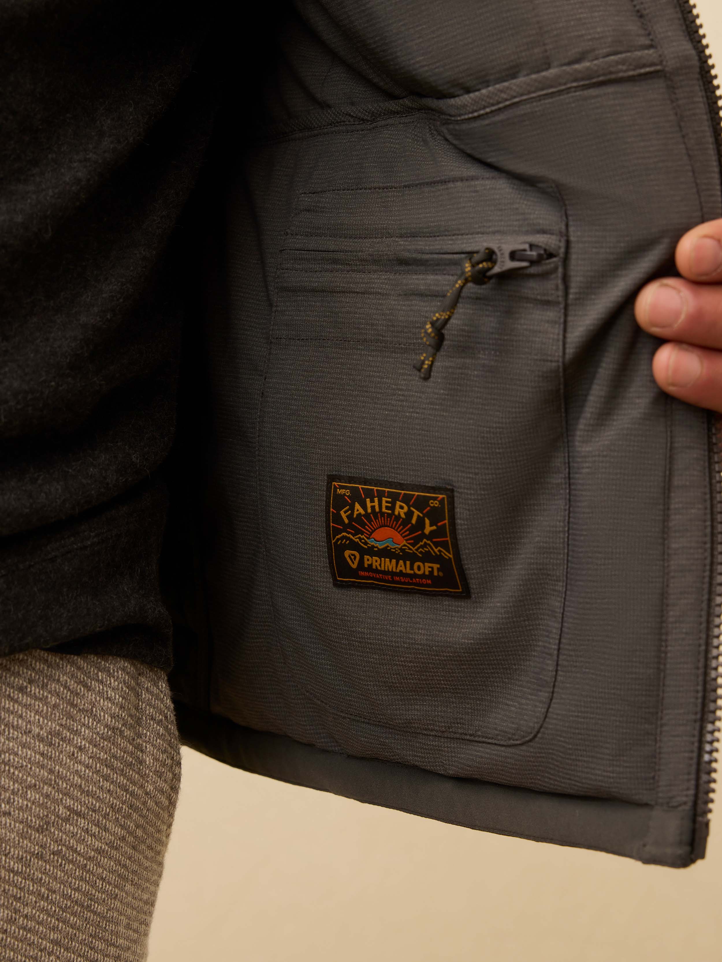 Close-up of a gray quilted vest with a Faherty brand patch on a beige background