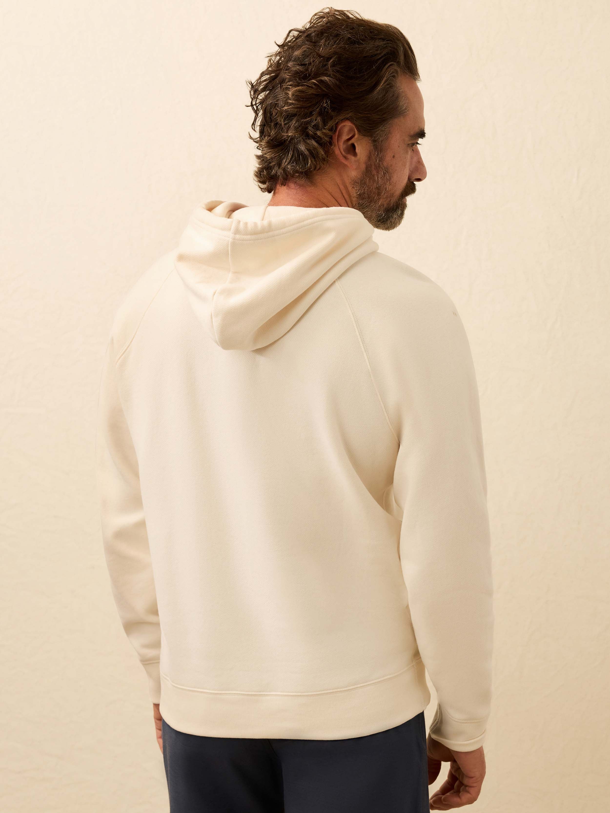 Man wearing a cream hoodie from behind on a beige background