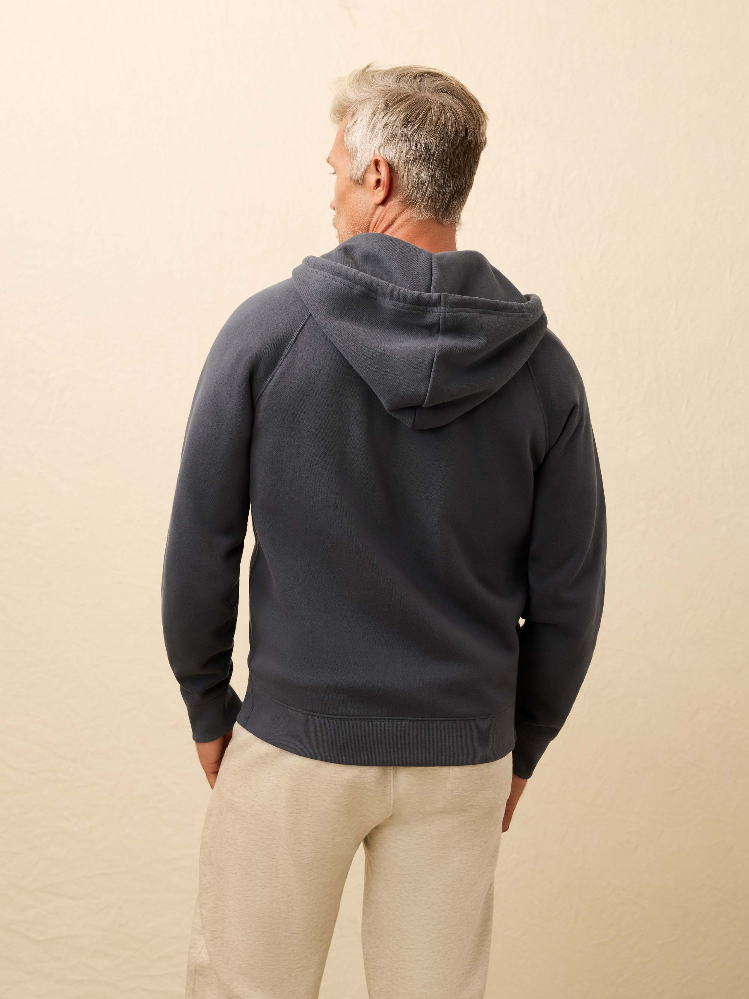 Man is wearing a navy zip hoodie against a beige background