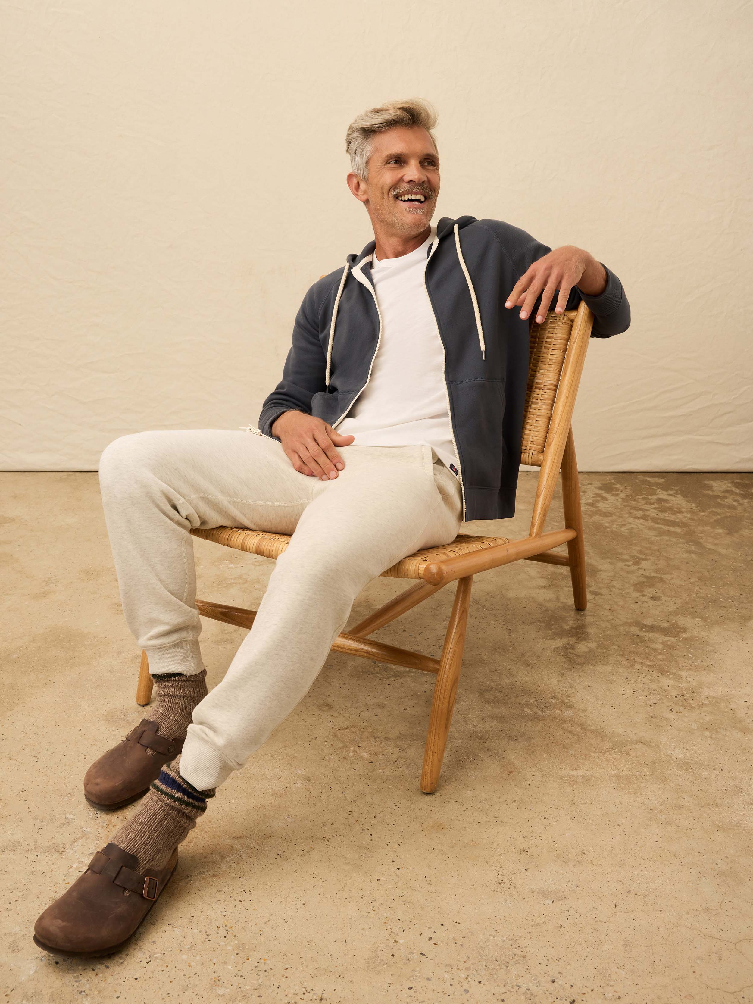 Man is wearing a navy zip hoodie layered over a white shirt against a beige background