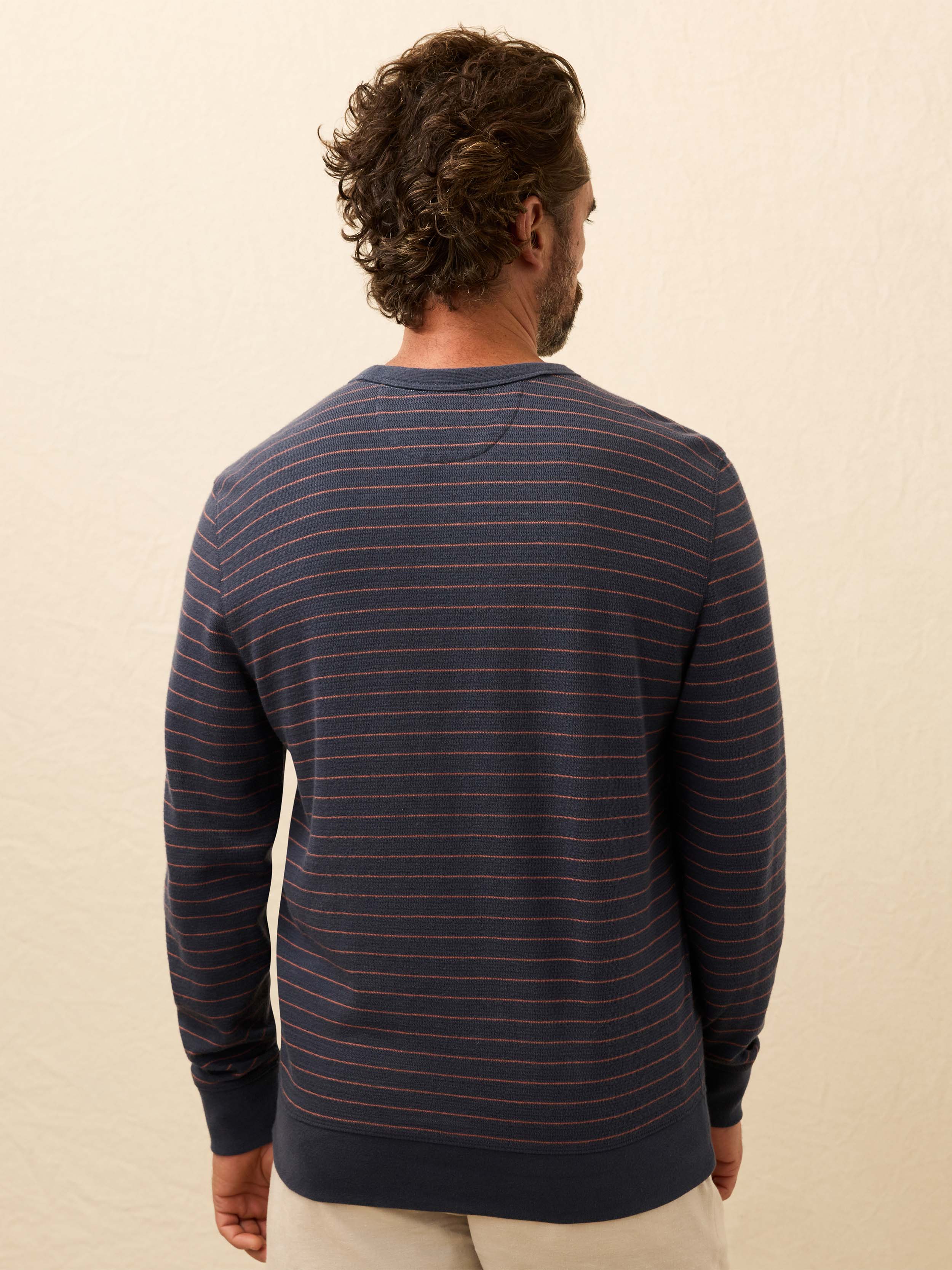 Man wearing a navy and red striped long sleeve shirt against a beige background