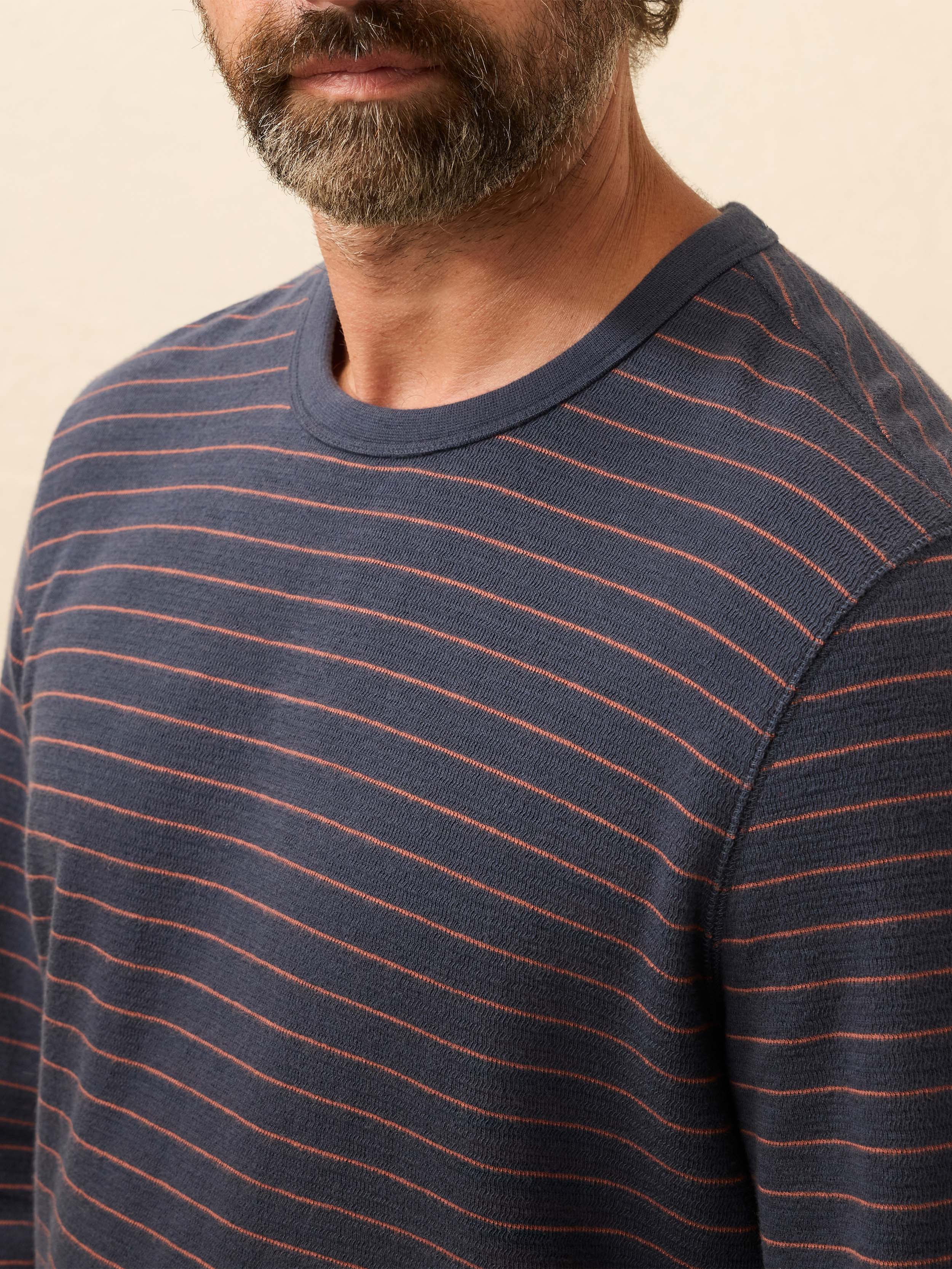 Man wearing a navy and red striped long sleeve shirt against a beige background