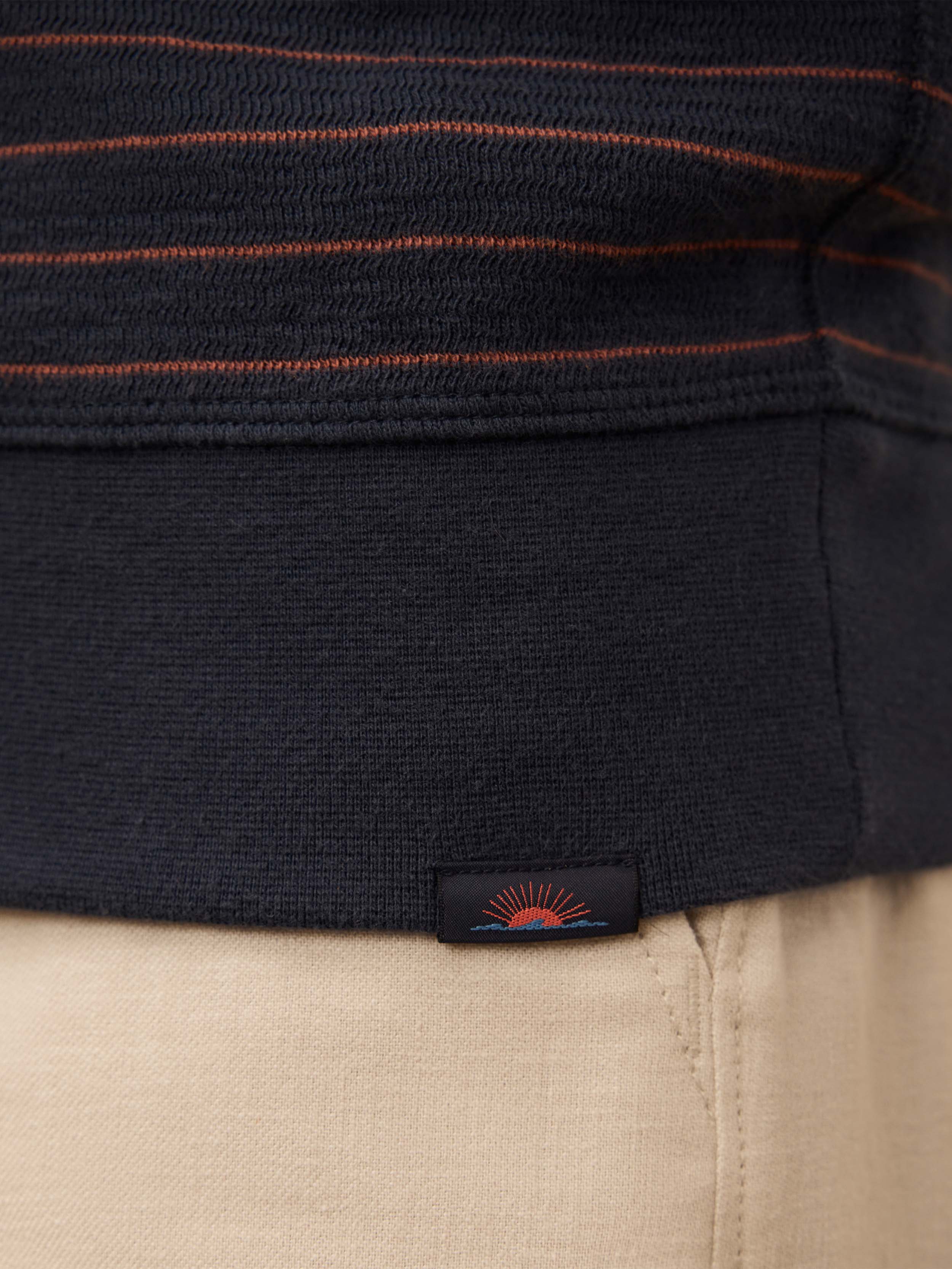 Close up of a blue and red striped shirt with a Faherty brand logo at the hem