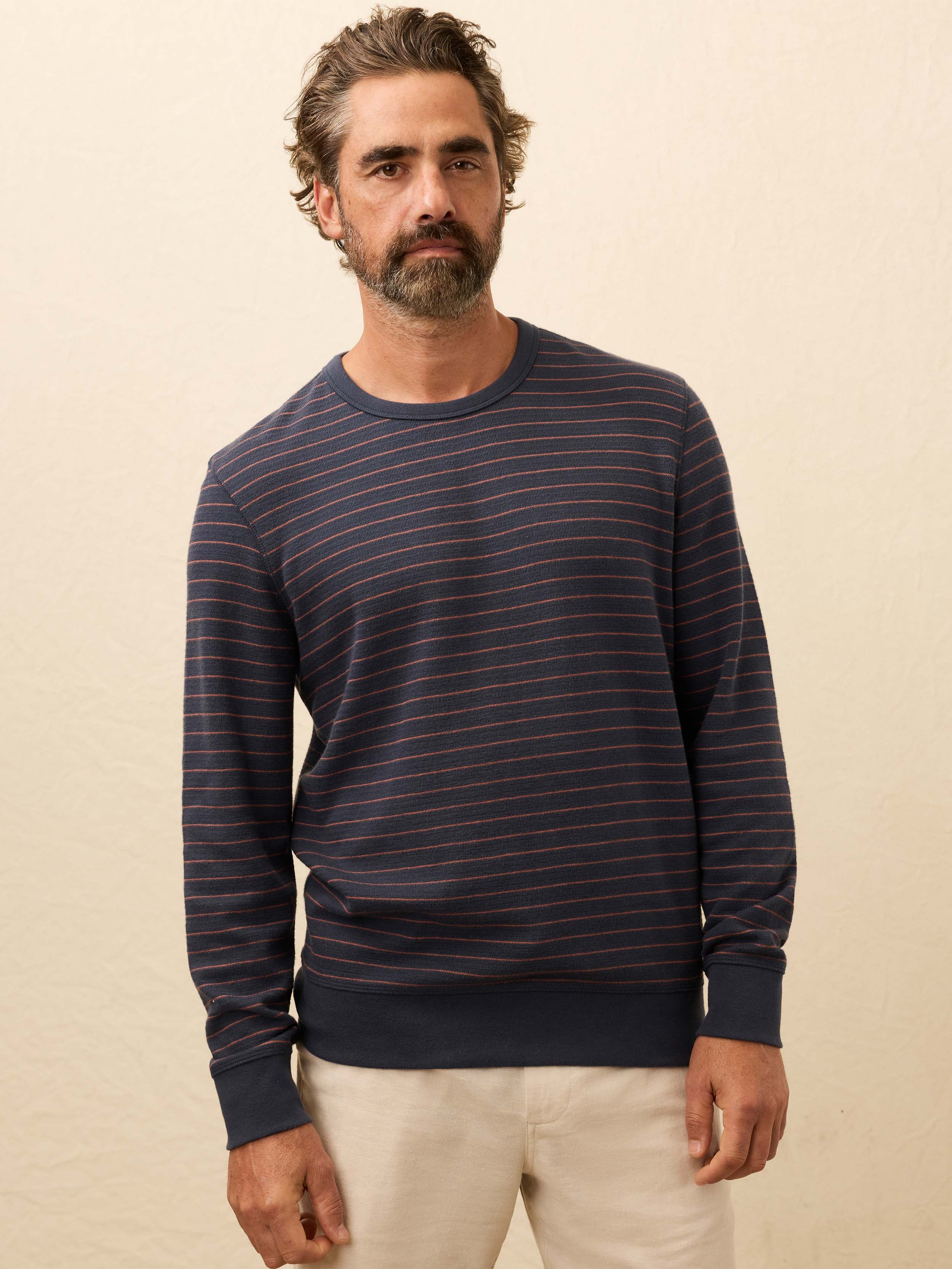 Man wearing a navy and red striped long sleeve shirt against a beige background