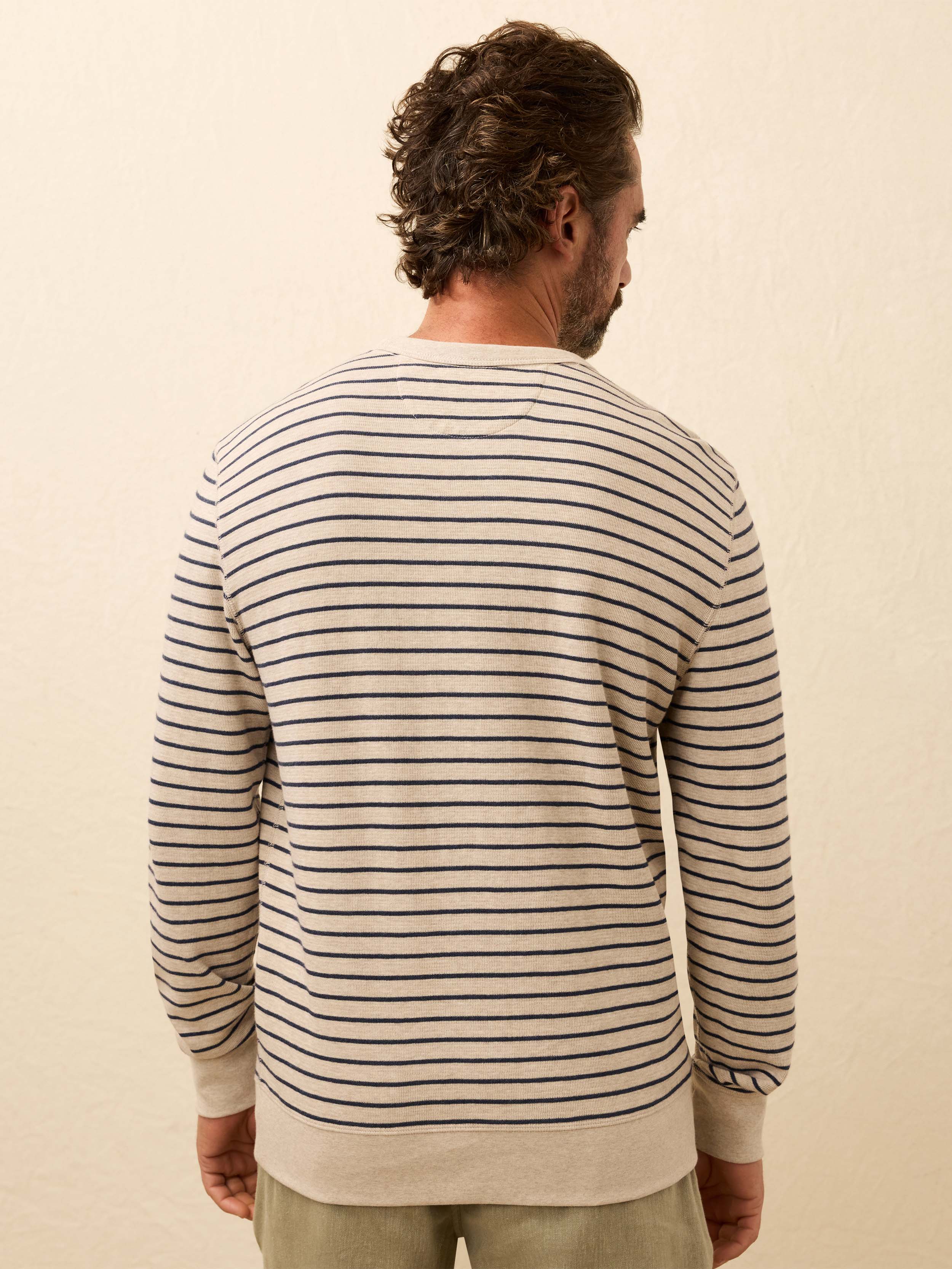 Man wearing a white and navy striped long sleeve crewneck against a beige background