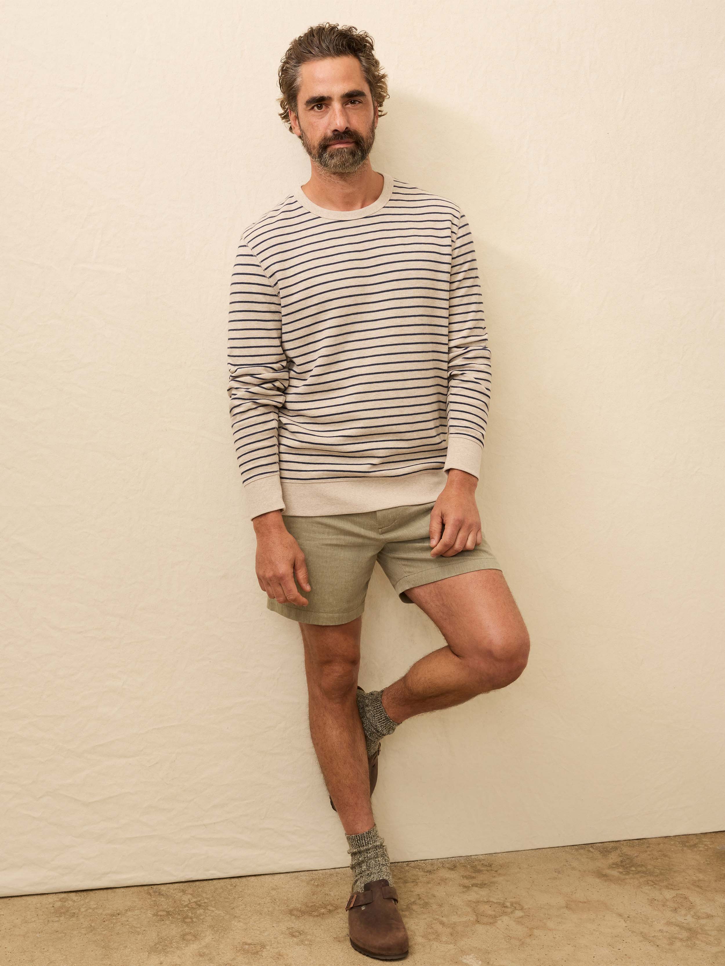 Man wearing a white and navy striped long sleeve crewneck against a beige background