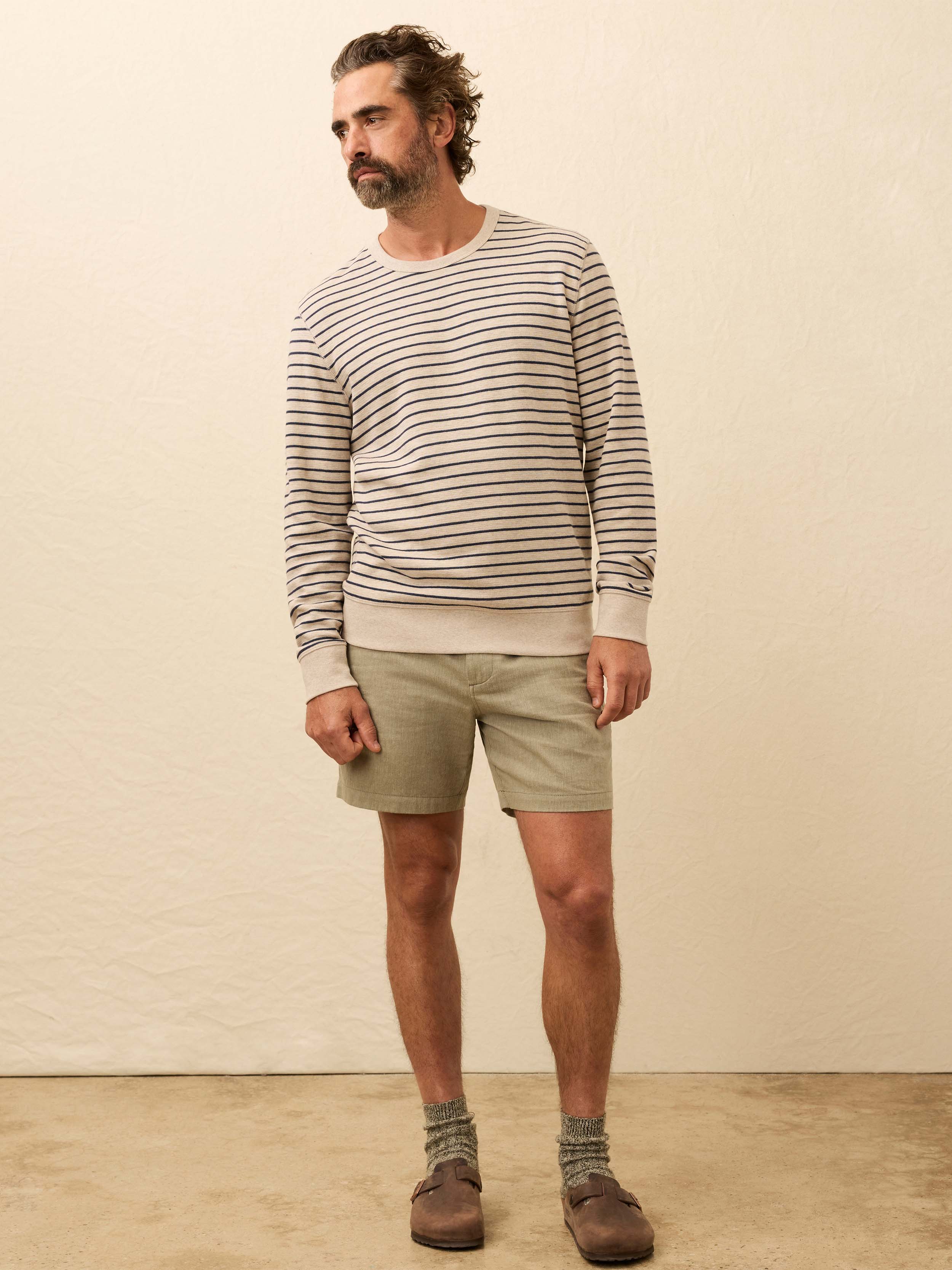 Man wearing a white and navy striped long sleeve crewneck against a beige background