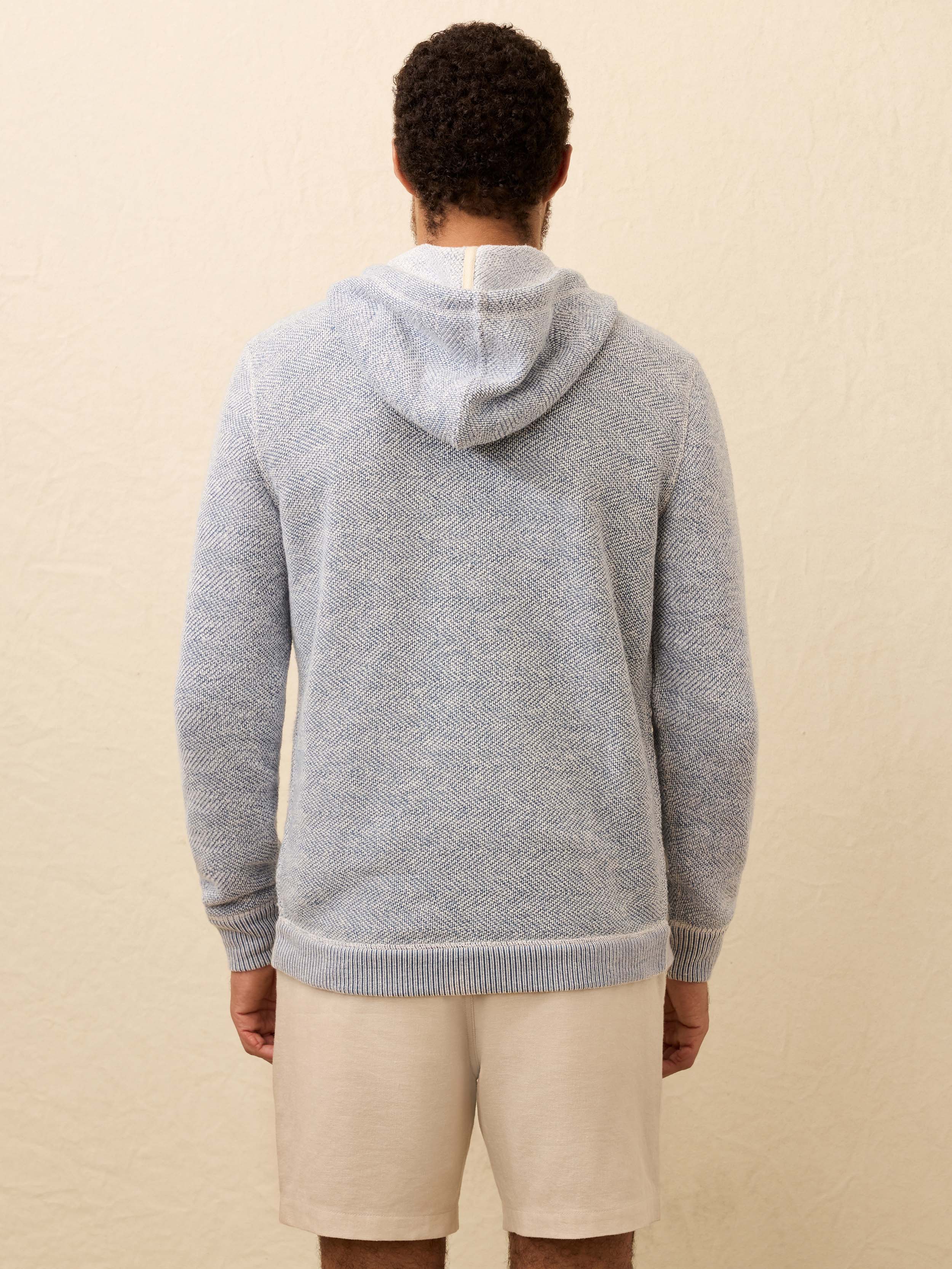 Back view of man wearing a blue hoodie and beige shorts against a beige background