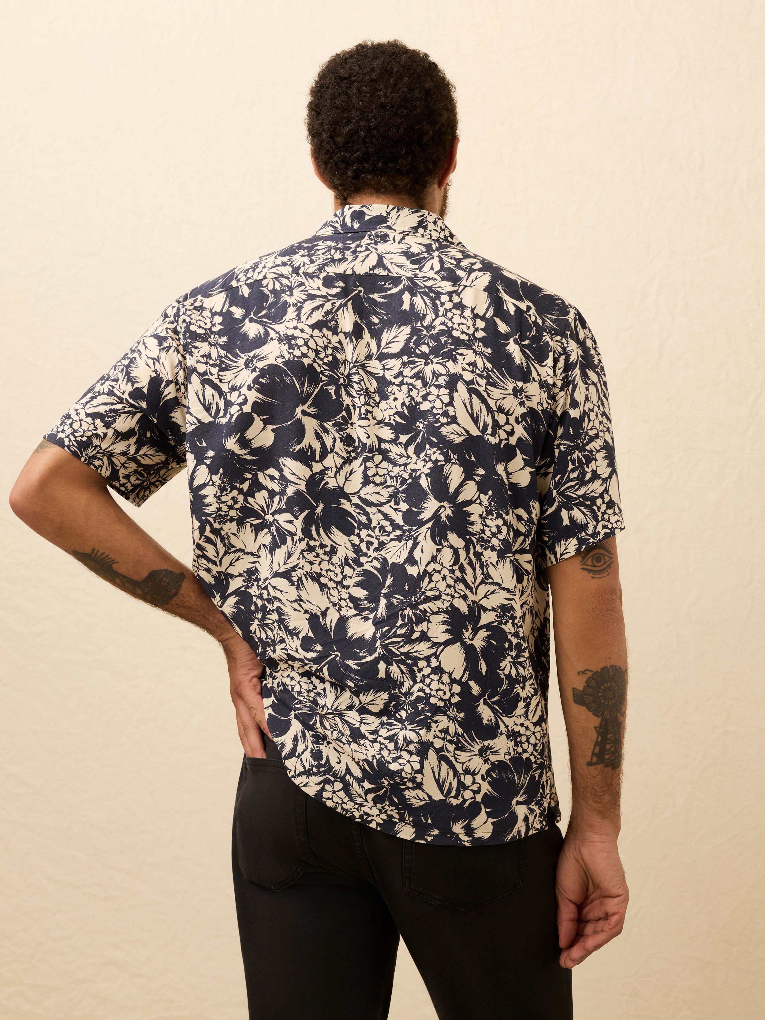 Man wearing a navy and cream floral shirt against a beige background