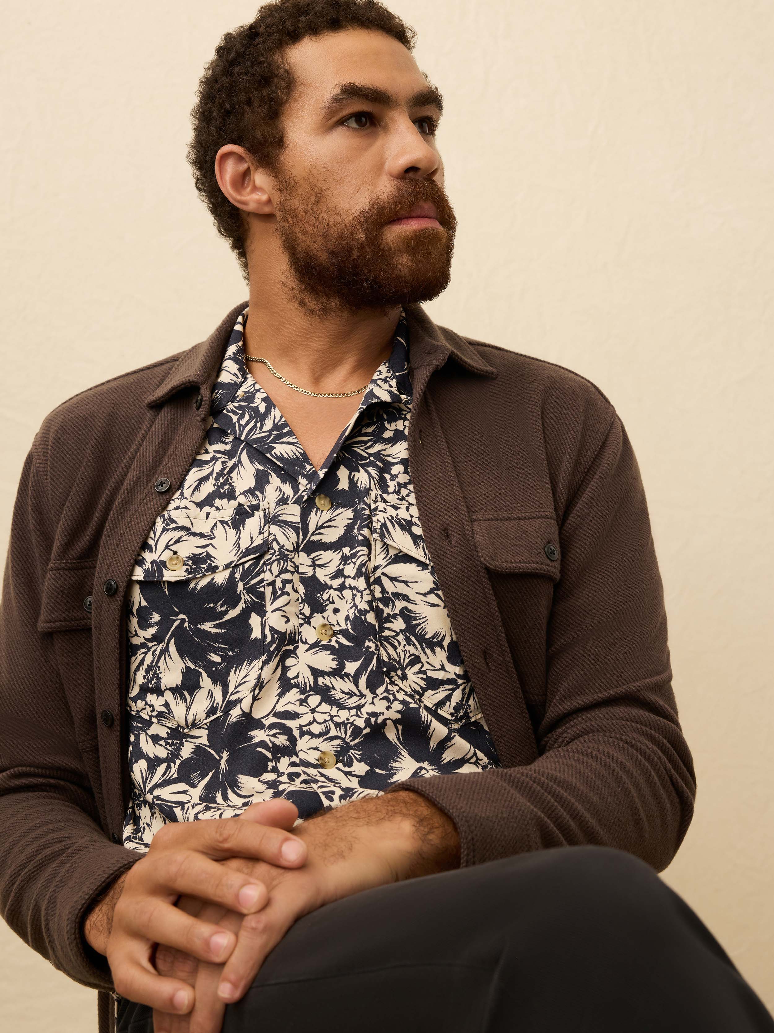 Man wearing a navy and cream floral shirt against a beige background