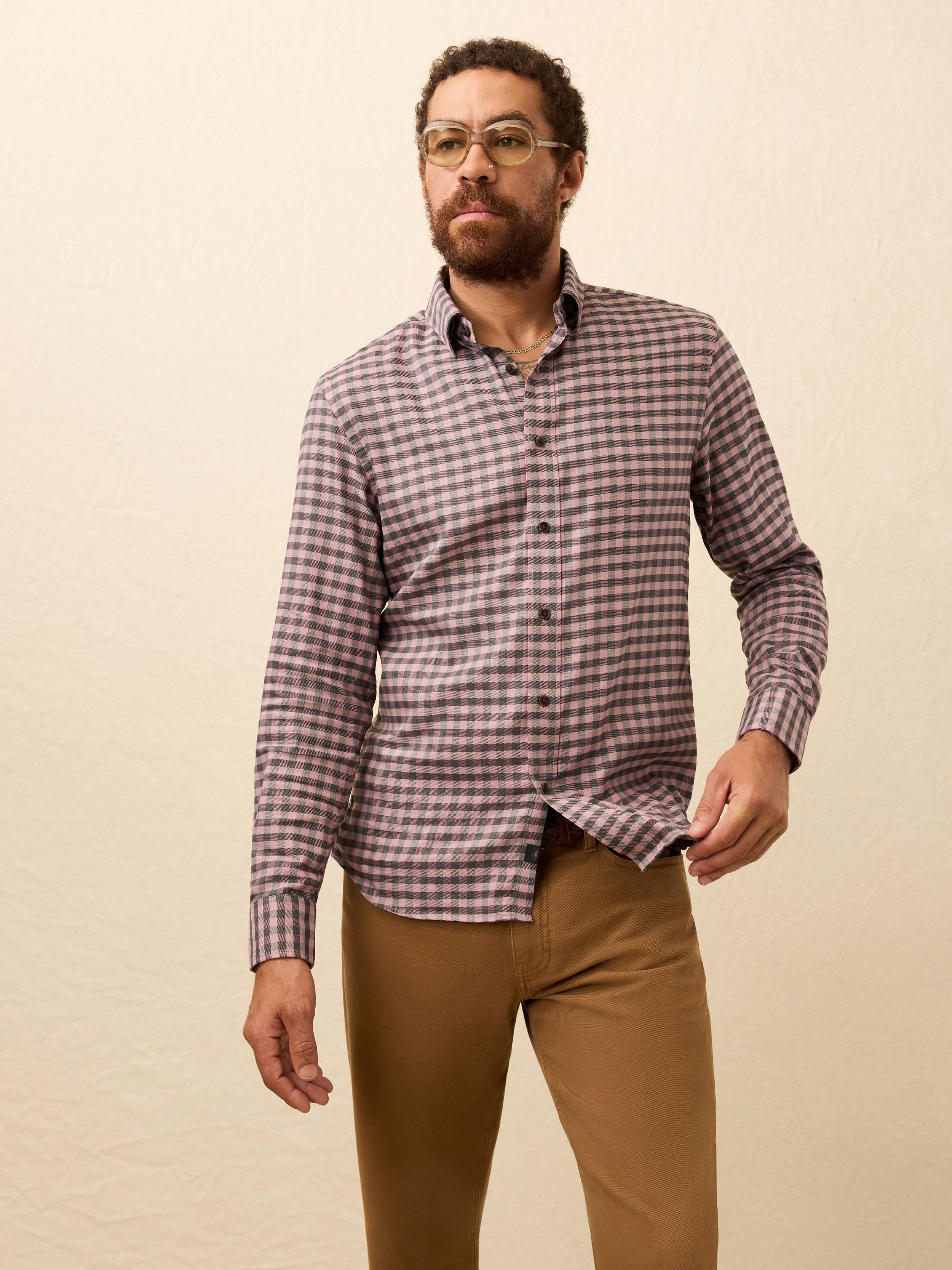 Man wearing a pink and grey gingham shirt and brown pants against a beige background