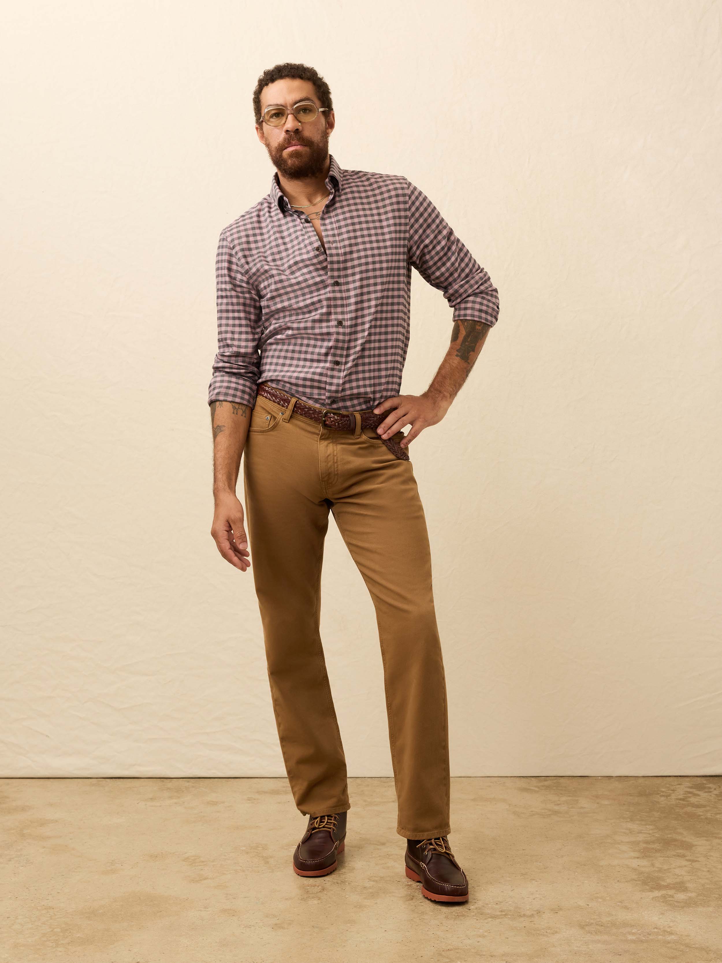 Man wearing a pink and grey gingham shirt and brown pants against a beige background