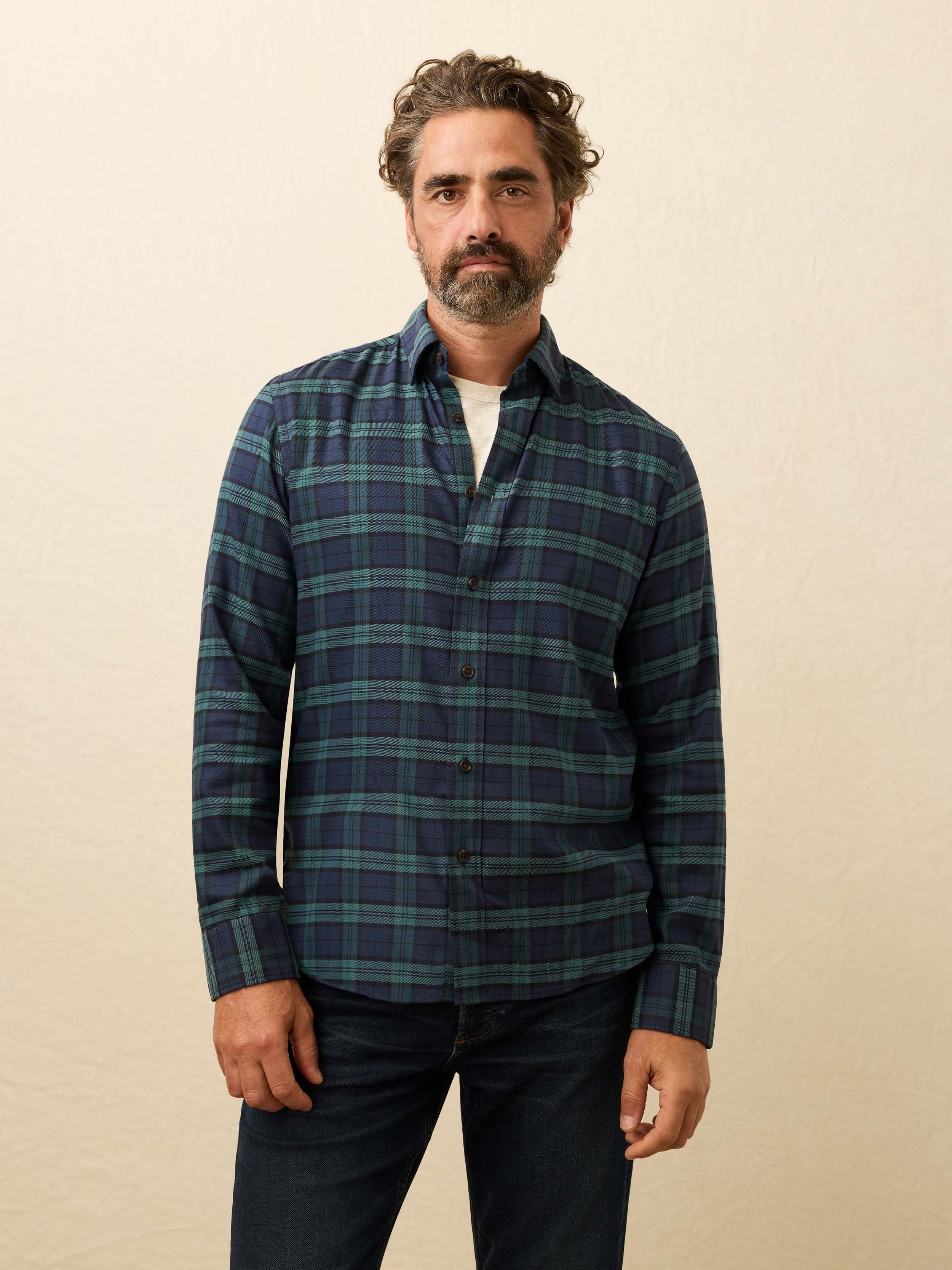 Man wearing a blue and green plaid shirt and jeans against a beige background