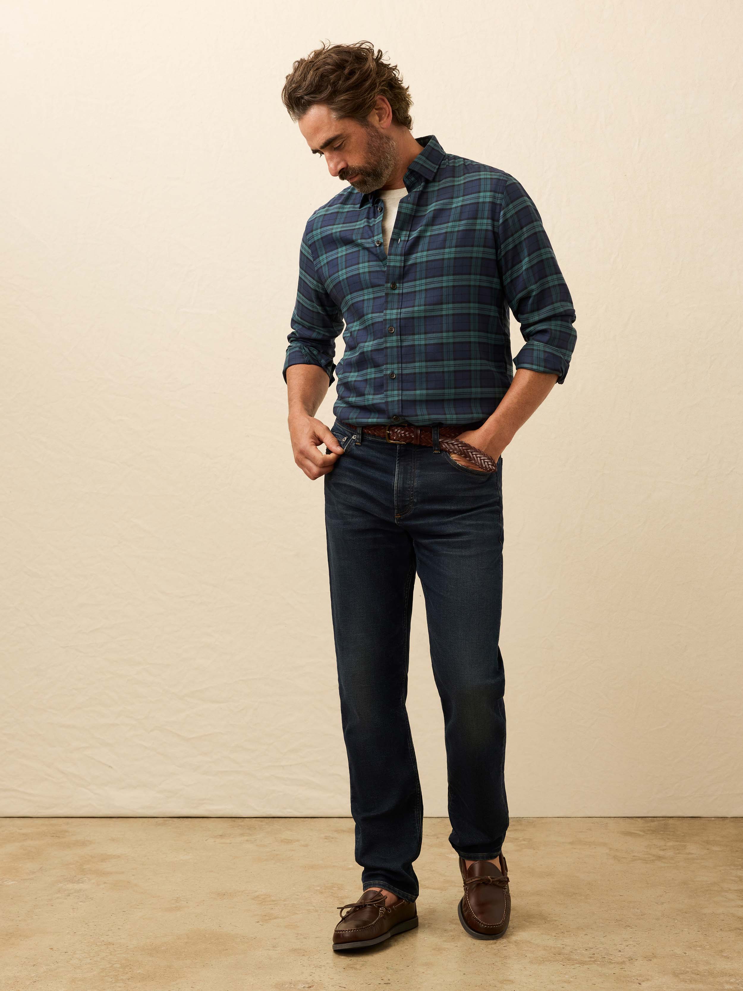 Man wearing a blue and green plaid shirt and jeans against a beige background