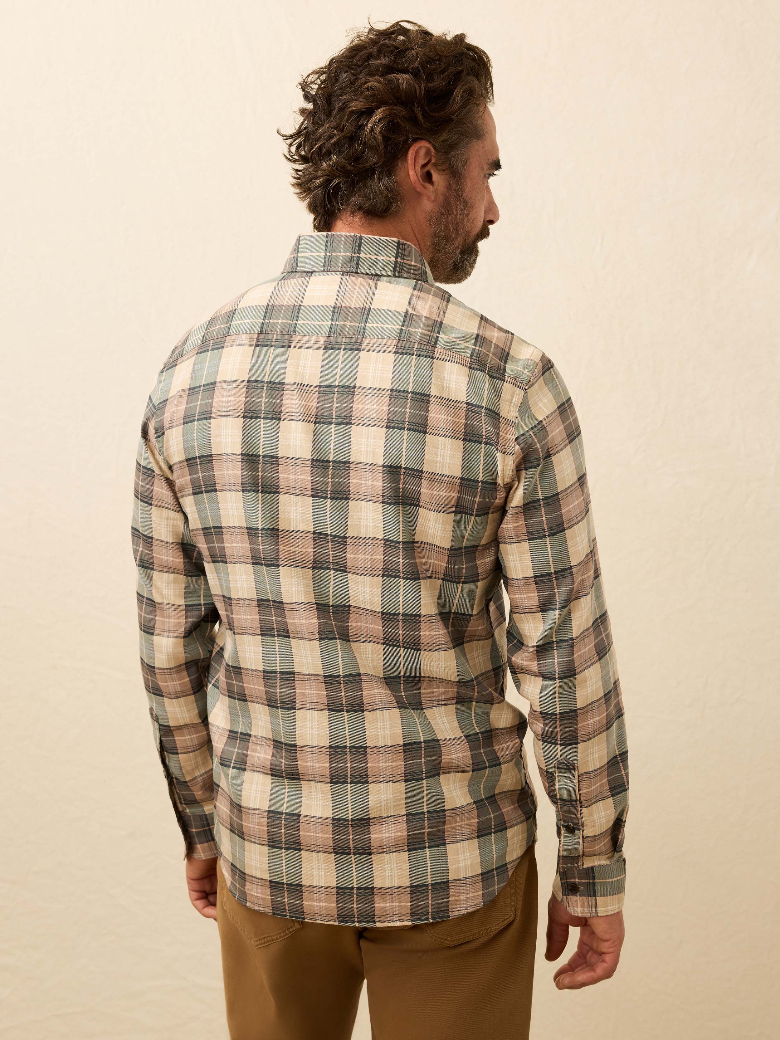 Man wearing a green and beige plaid shirt against a beige background