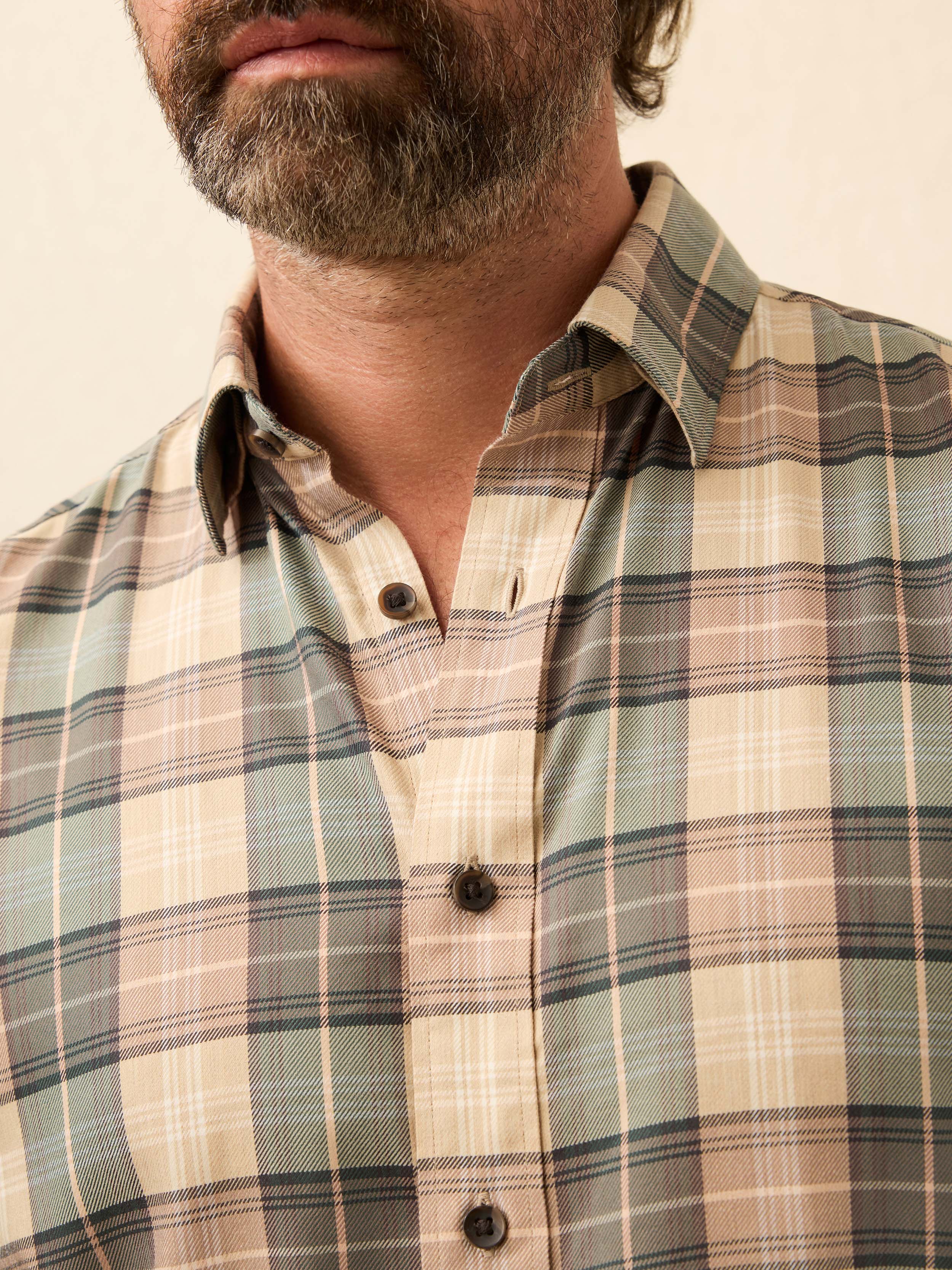 Man wearing a green and beige plaid shirt against a beige background