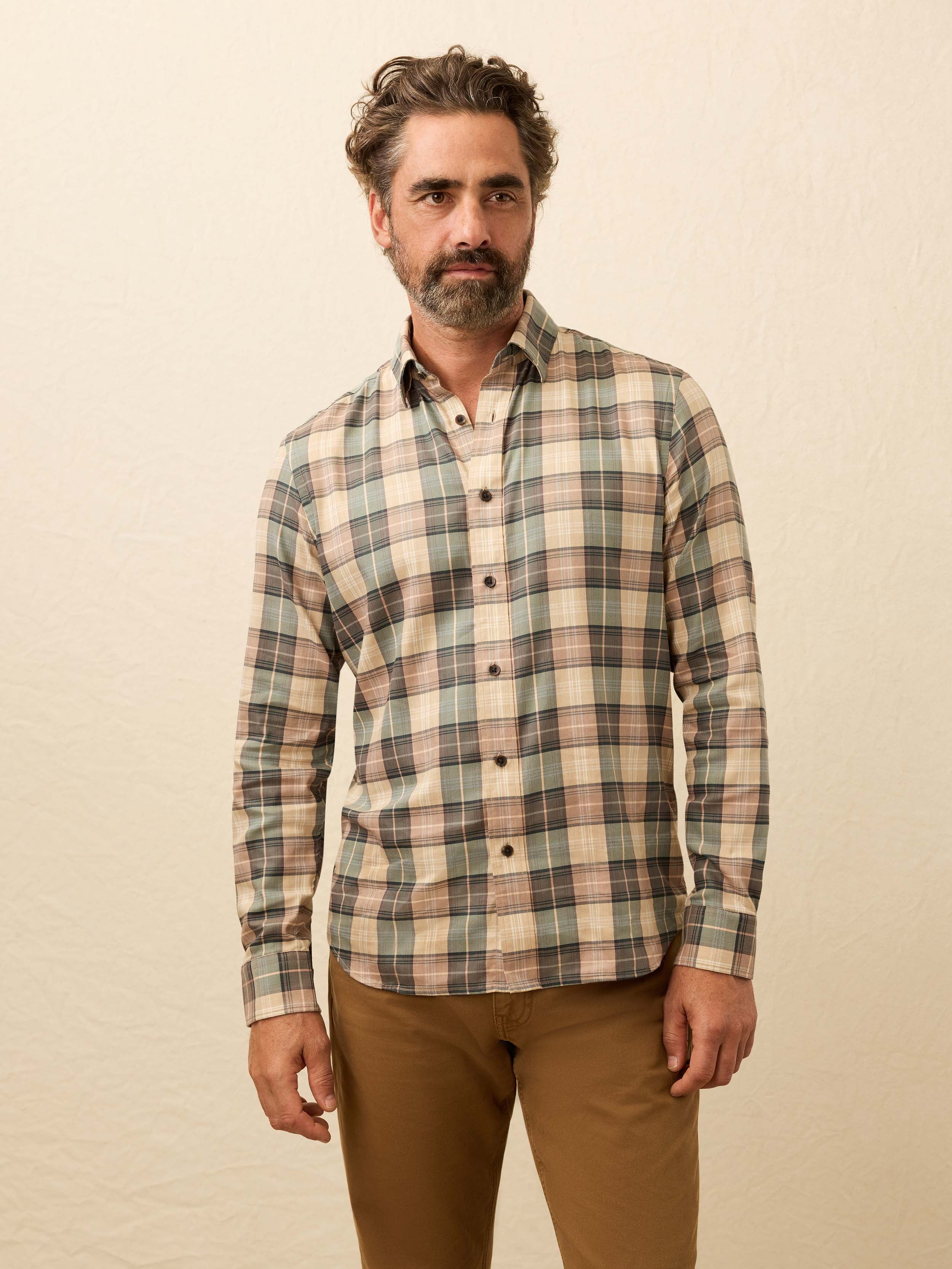 Man wearing a green and beige plaid shirt against a beige background