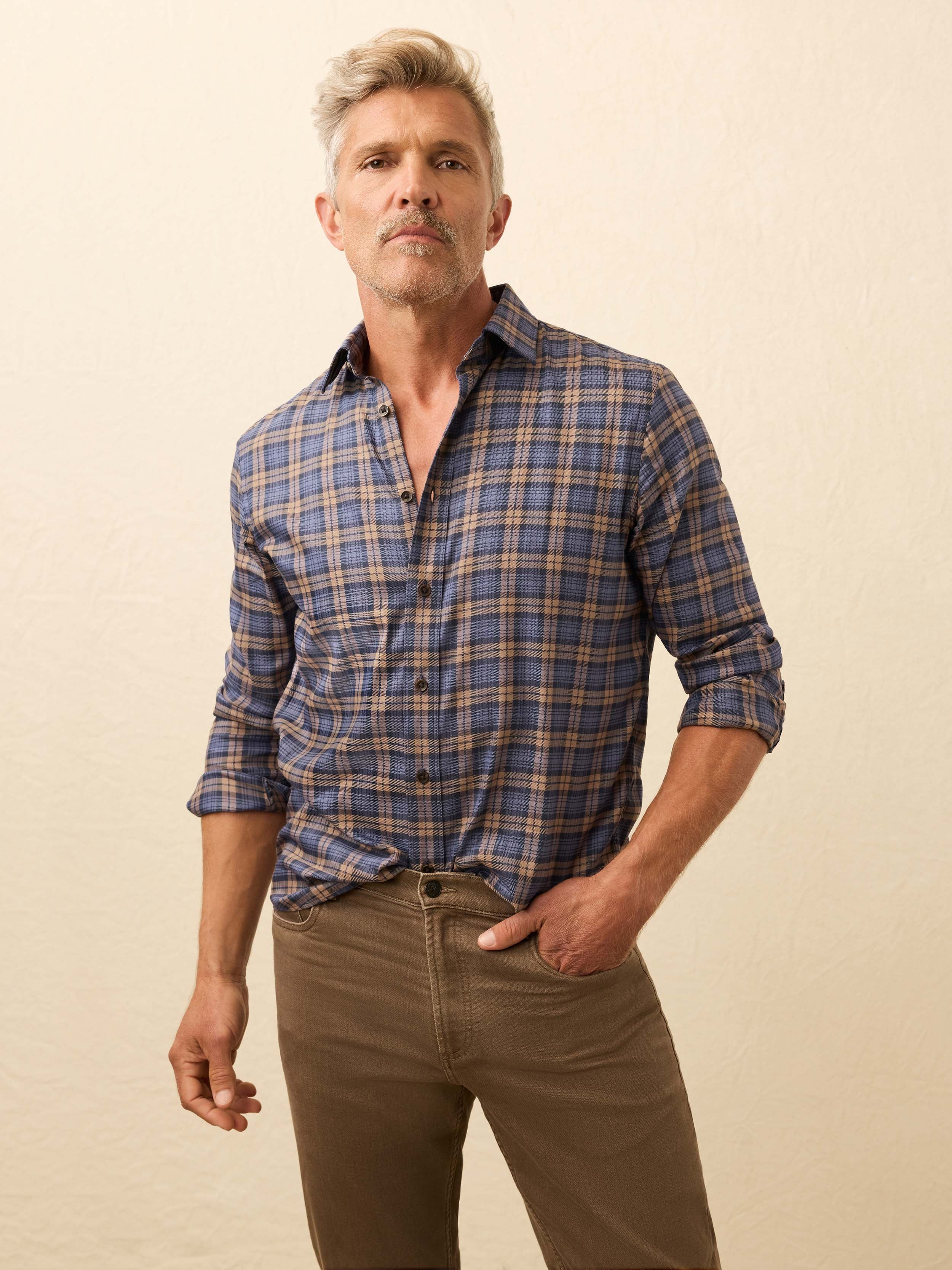 Man wearing a blue and yellow plaid shirt with brown pants against a beige background
