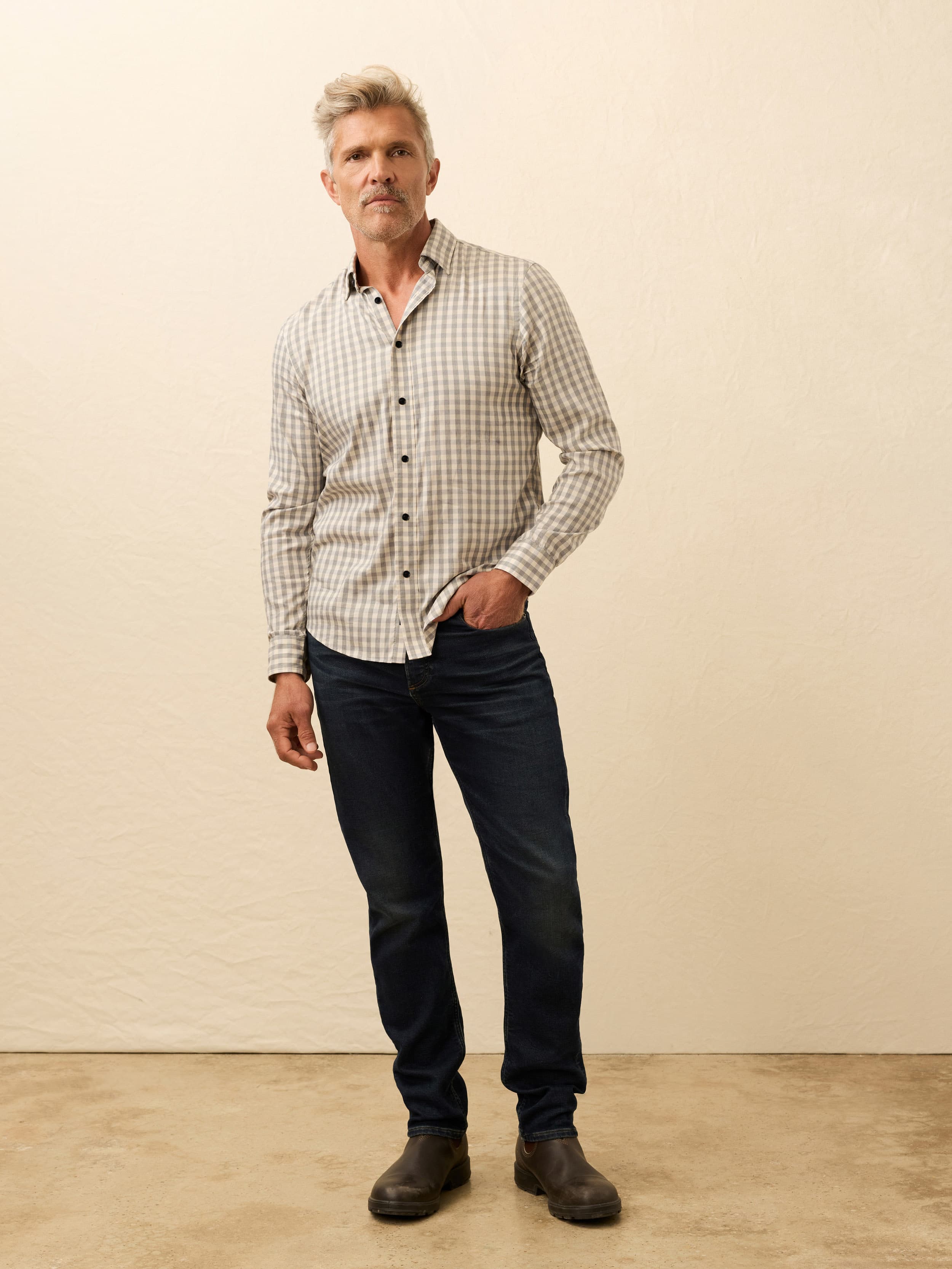 Man wearing a checkered shirt and dark jeans against a beige background