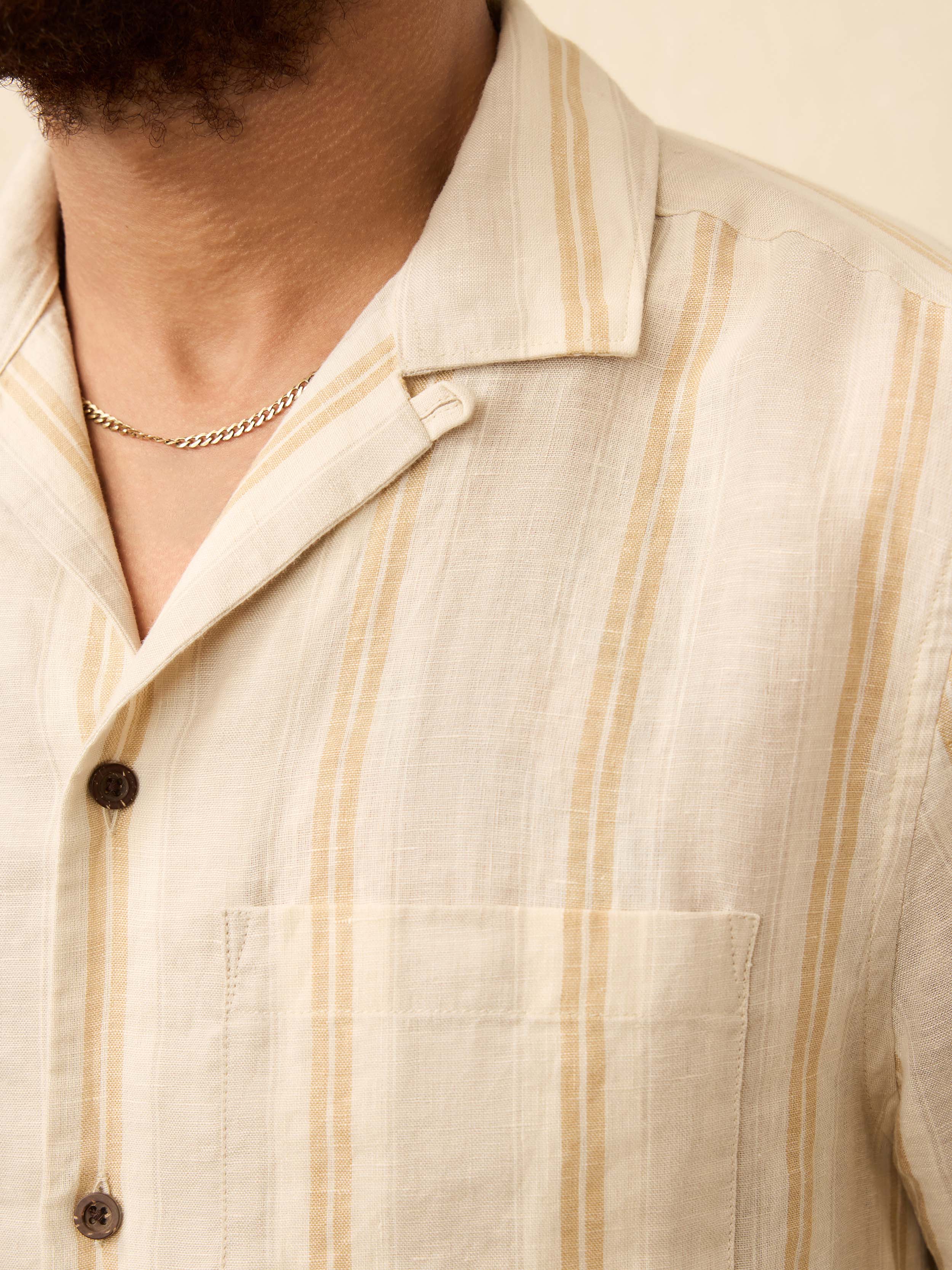 Close up of a man wearing a cream shirt with orange stripes against a beige background