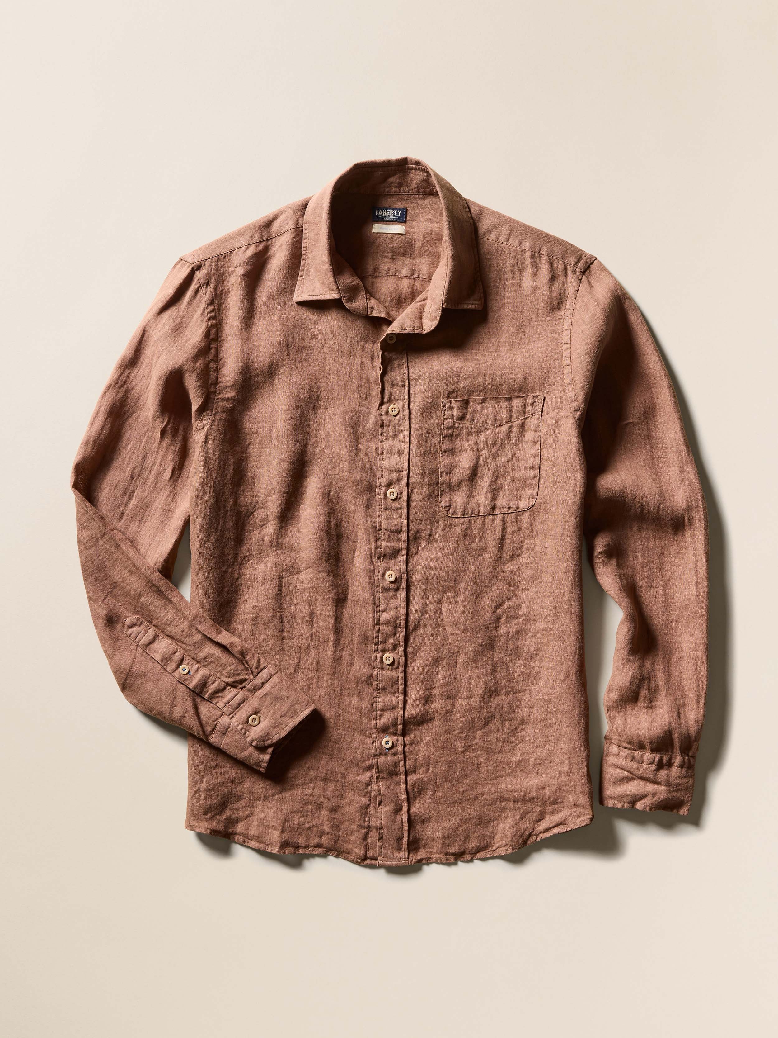 Flat image of a burnt orange long-sleeve button-up shirt on a beige background